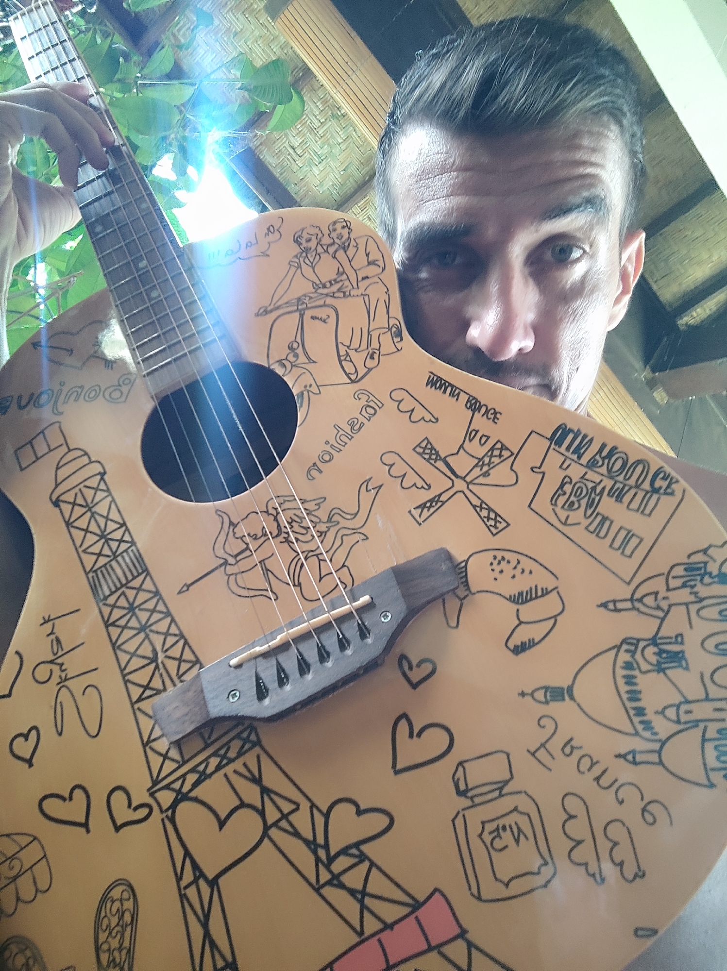 Man poses with Paris-decorated guitar in Ubud, Indonesia