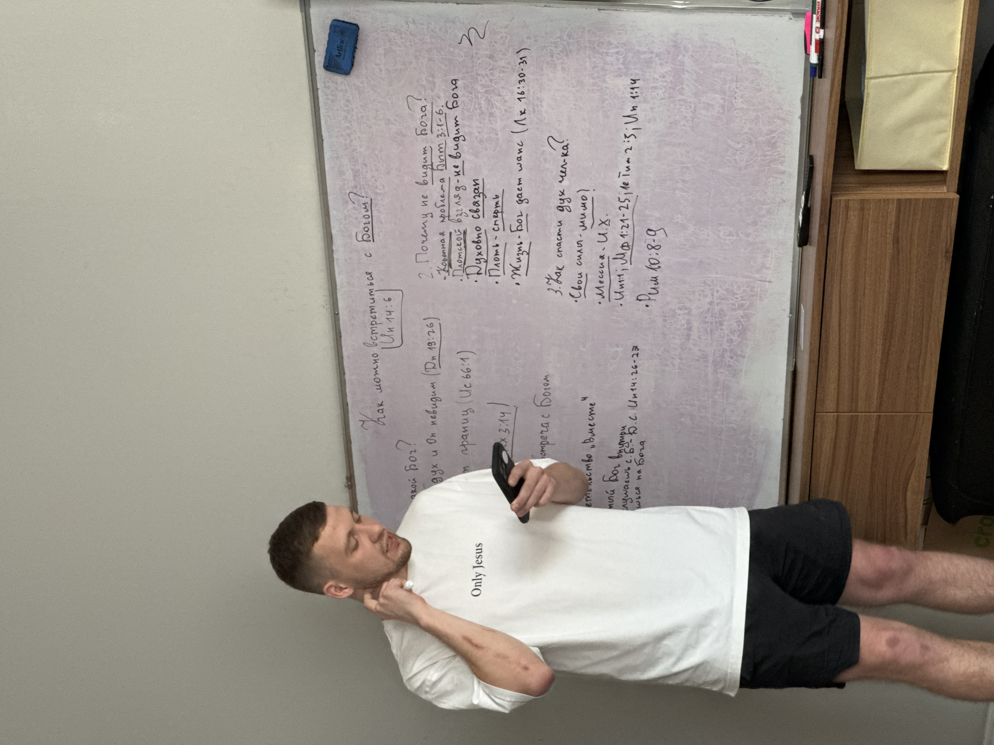 Man with religious shirt stands near Cyrillic whiteboard in Kerobokan