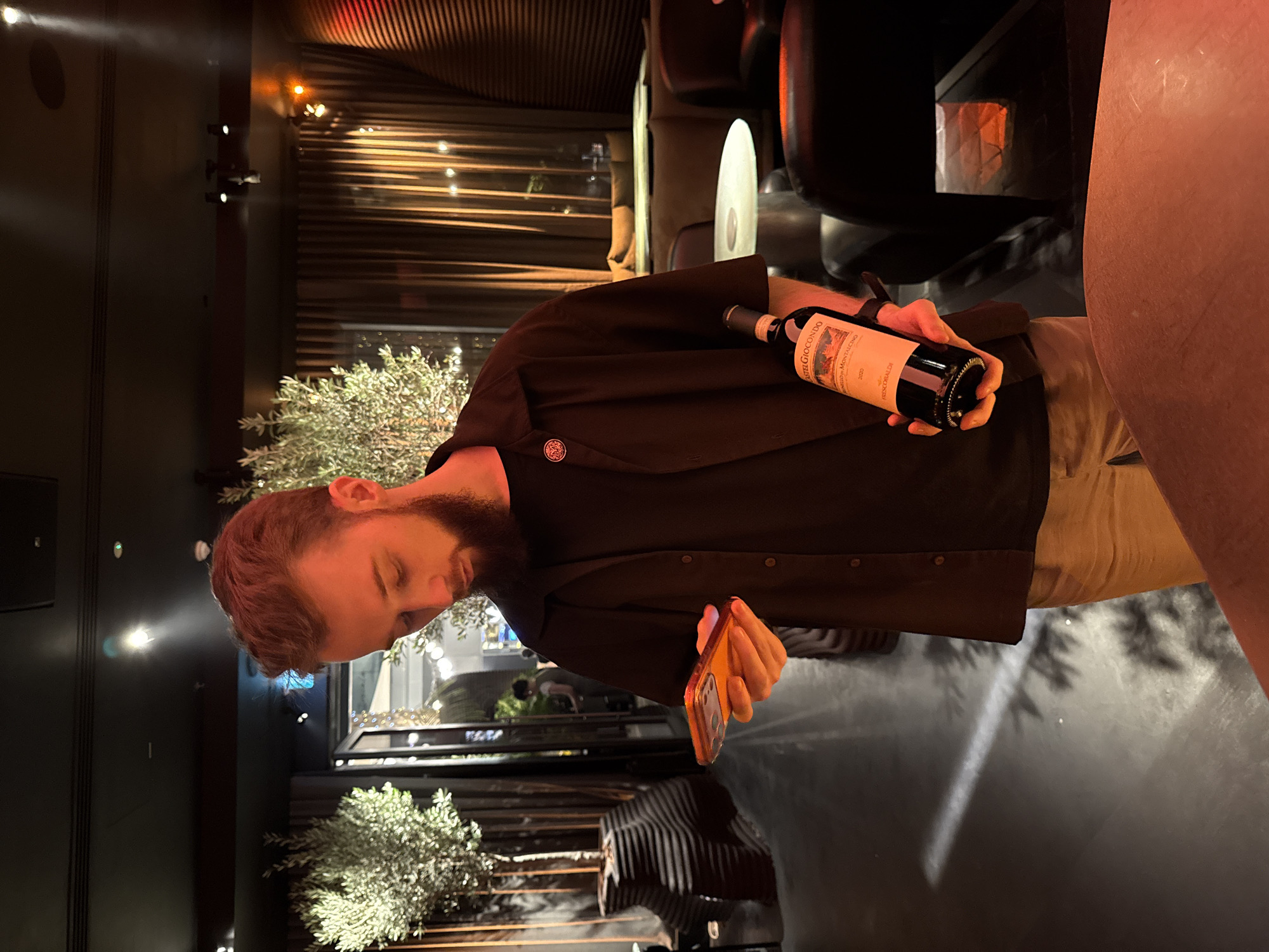 Man holds wine bottle and phone indoors in Dubai