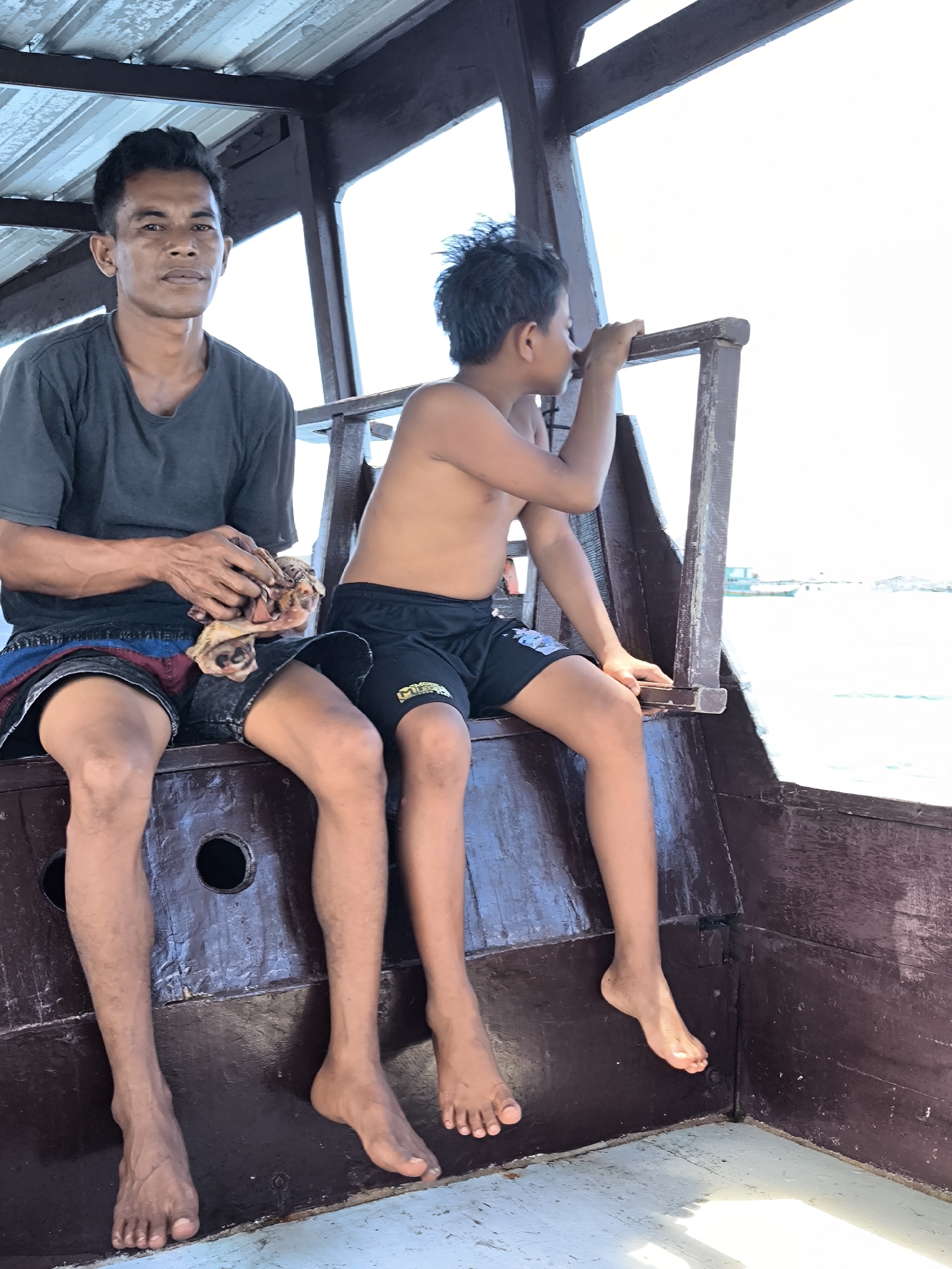 Two men sit on wooden boat in Labuan Jambu