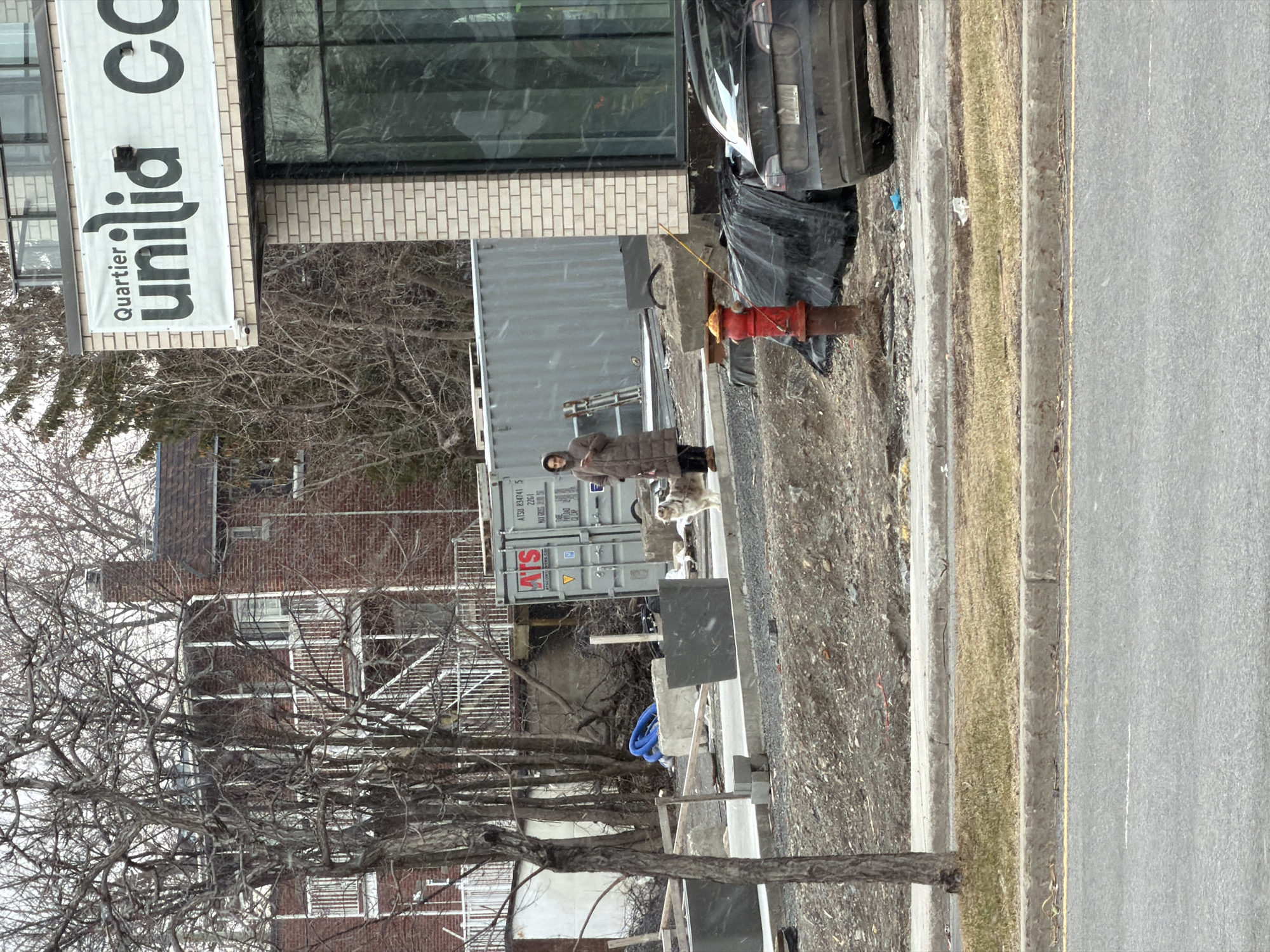 Woman walks white dog near construction site in Laval