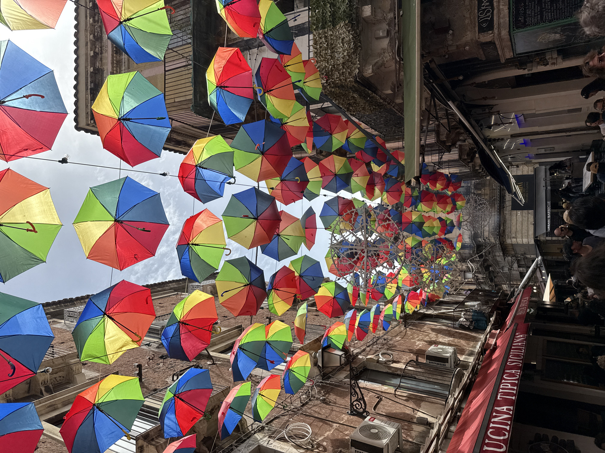Colorful umbrellas suspended over Catania street scene observed