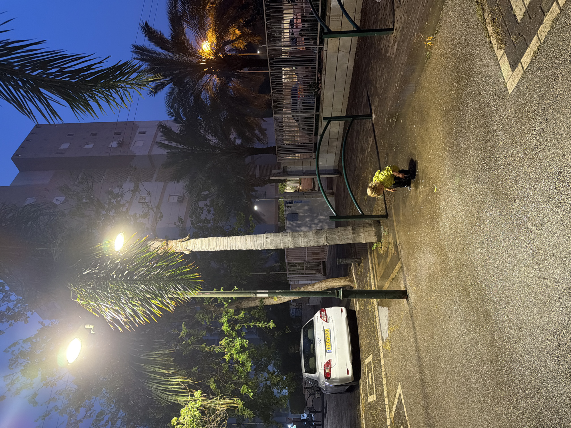 Child plays in wet Kiryat Bialik square at dusk