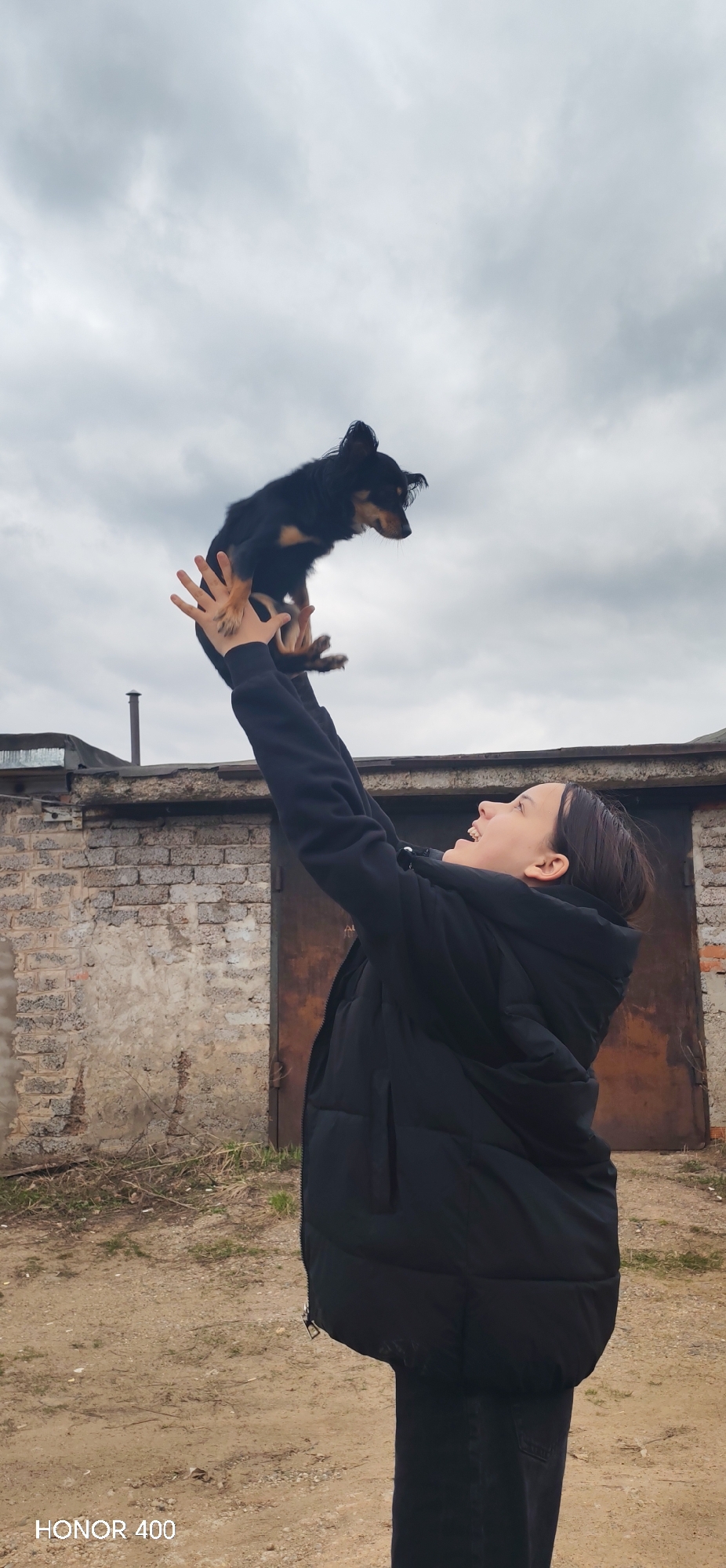 Woman plays with small dog outside garages in Noviy, Russia