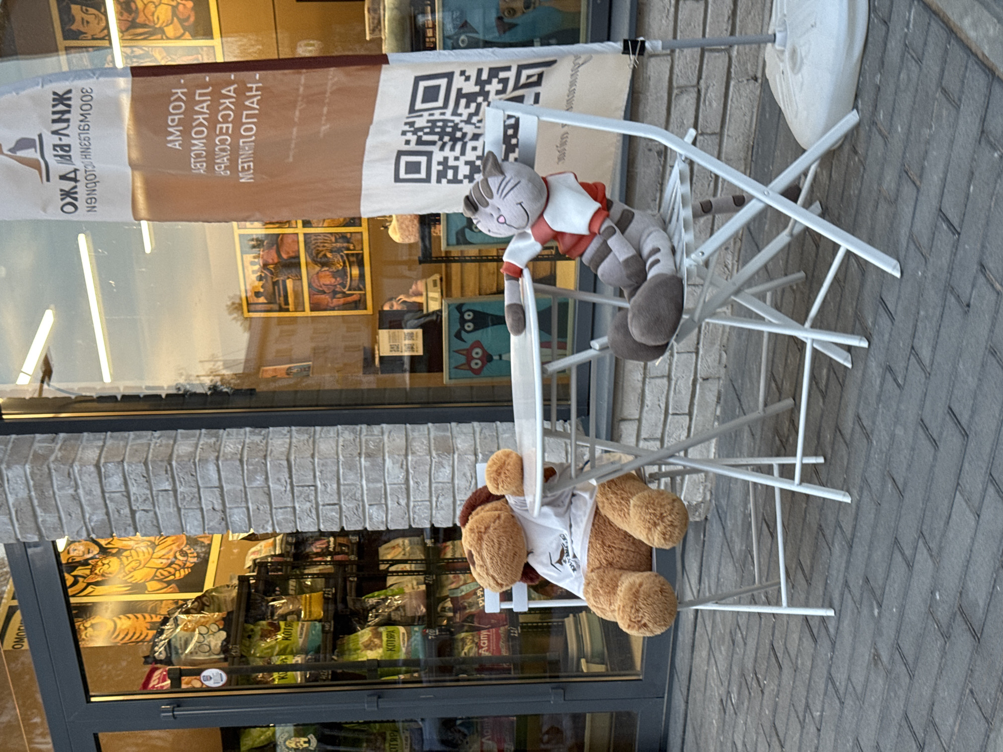Plush toys at a sidewalk table, contrail over Izhevsk