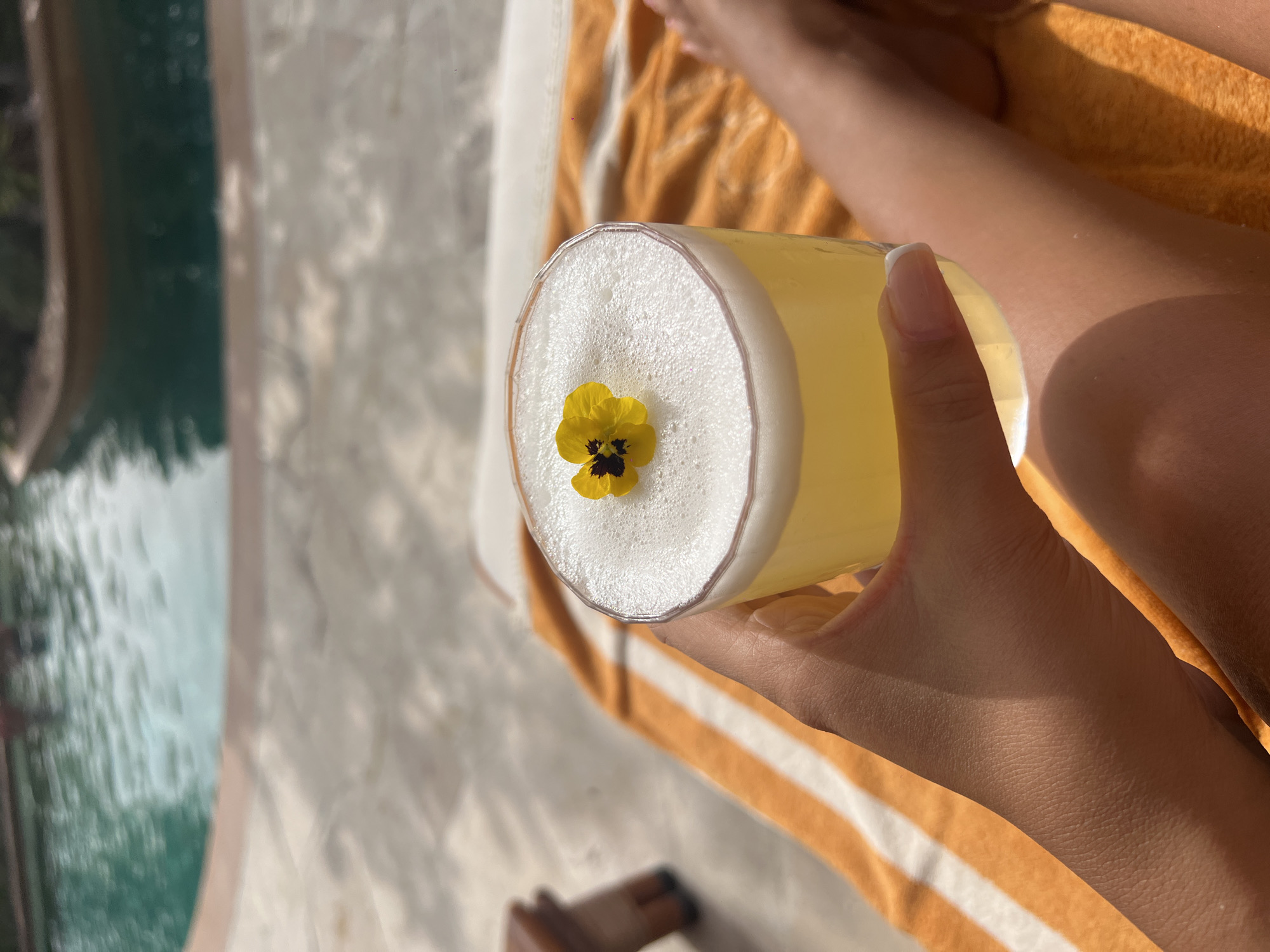 Person enjoys yellow cocktail with flower garnish in Dubai