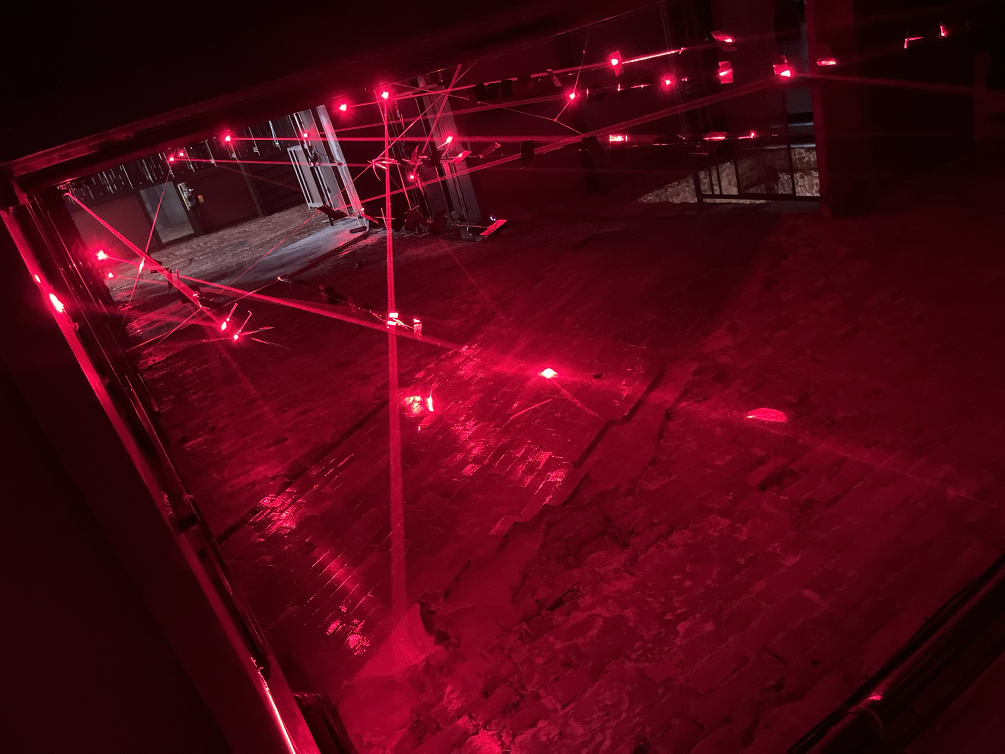 Red-lit installation space with lasers, crowds, and theatrical projections