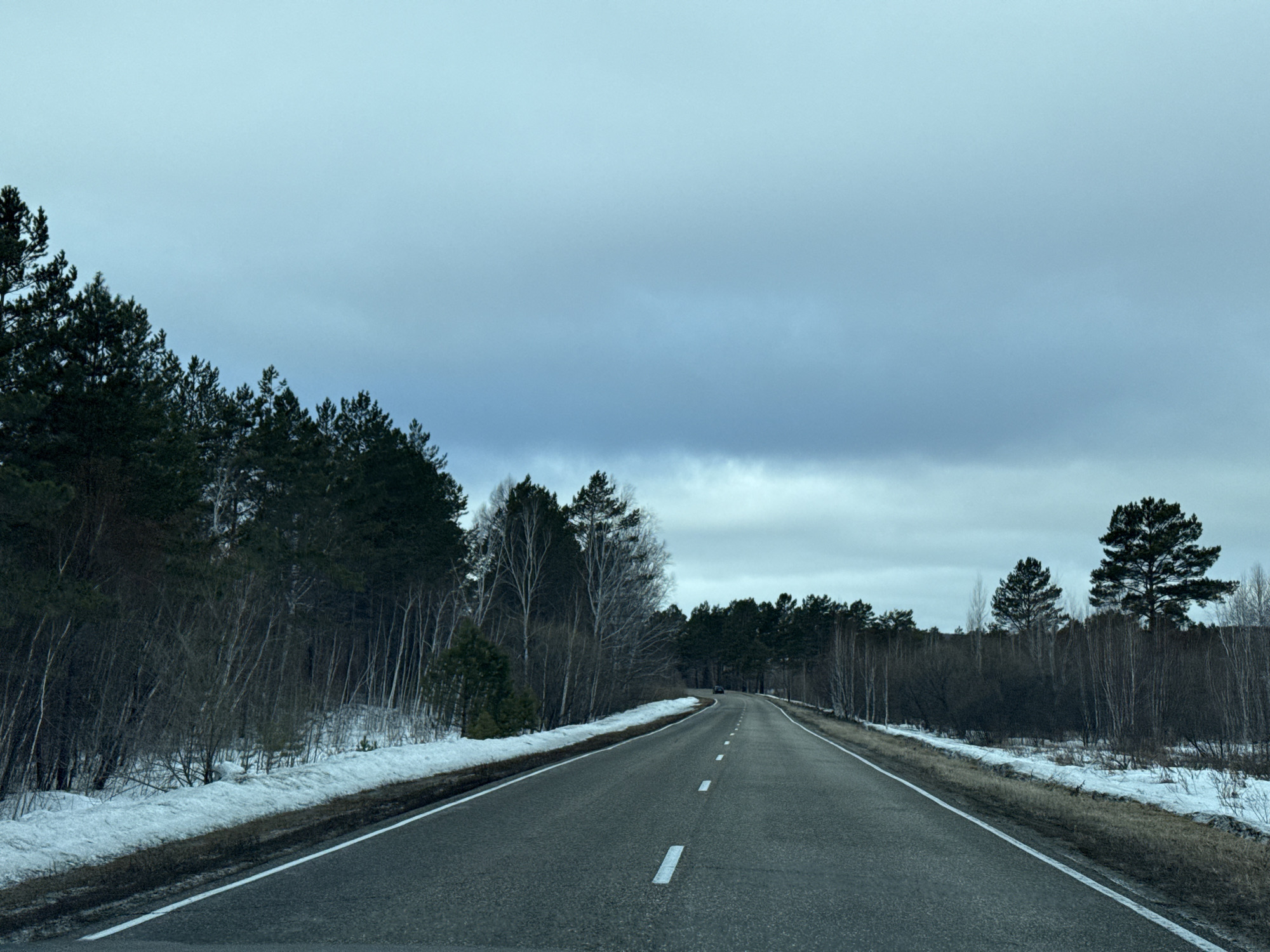 Vehicle travels winter road through forested mountainous terrain