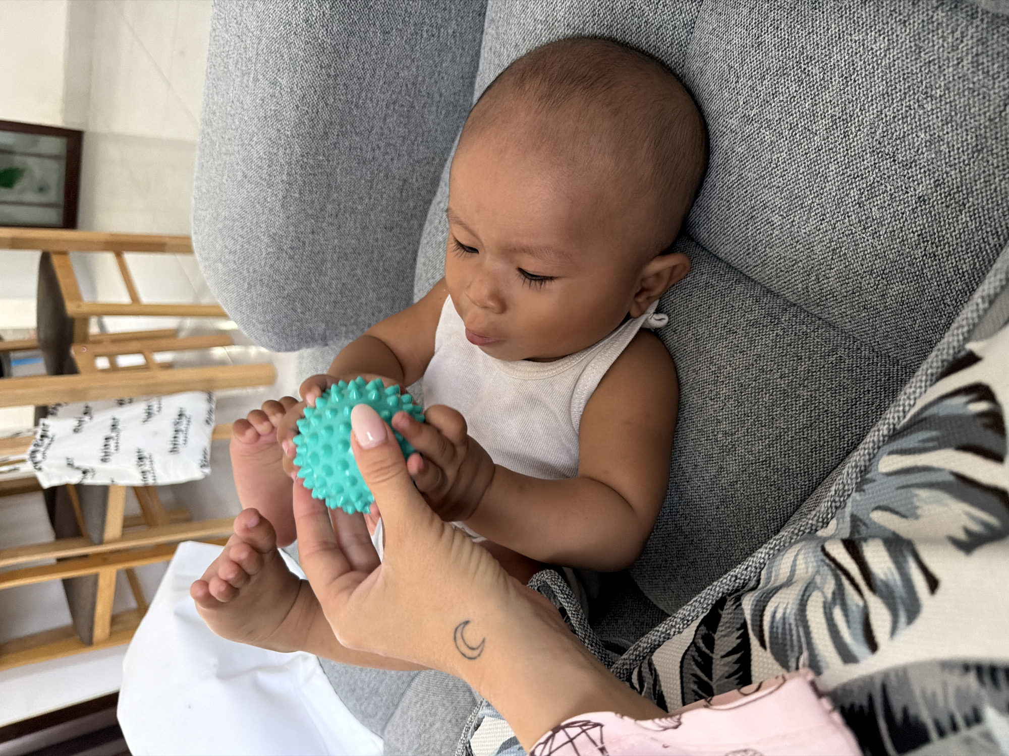 Baby and Pomeranian share a couch with a teal spiky ball