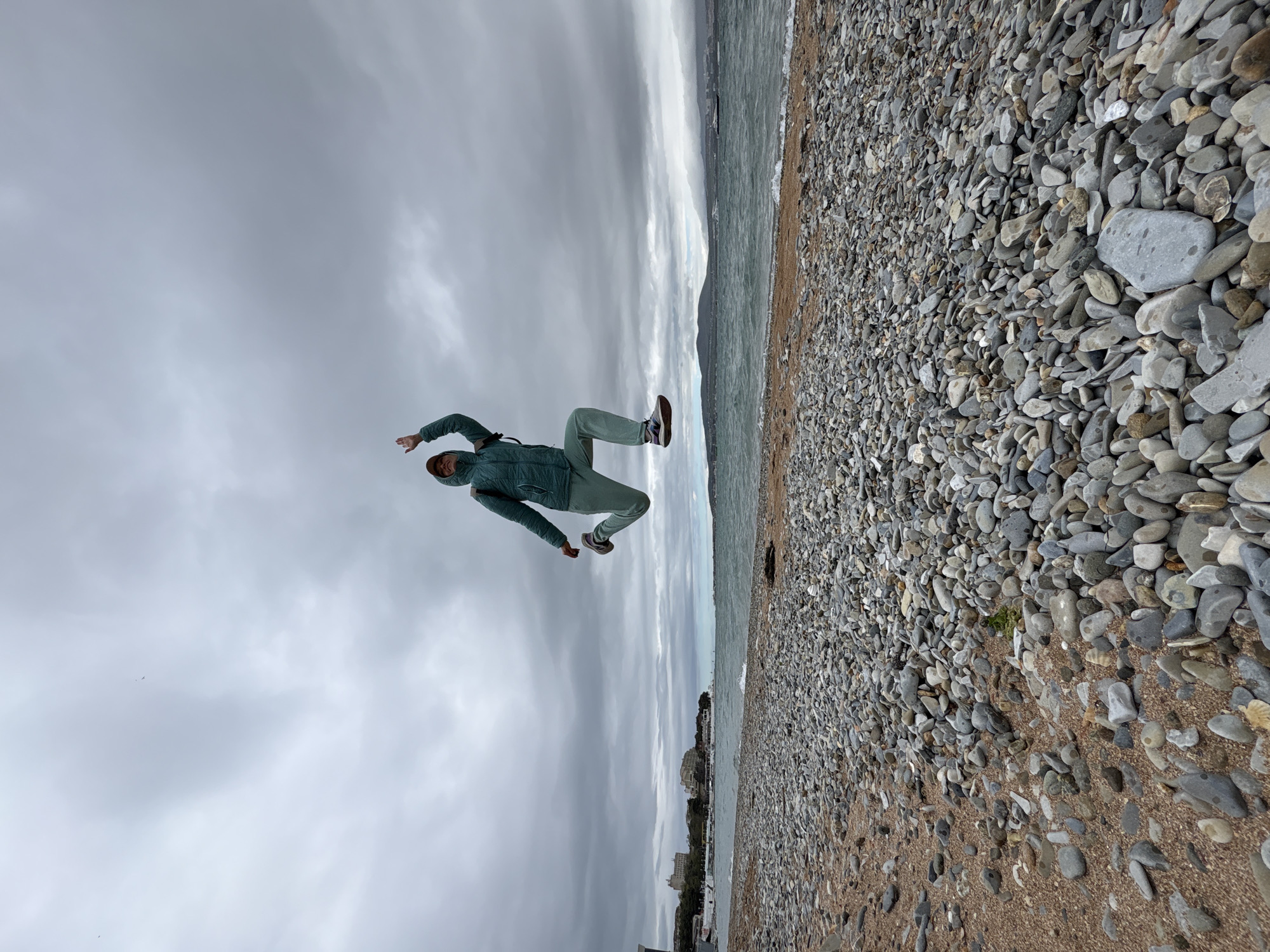 Person jumps on pebble beach in green tracksuit