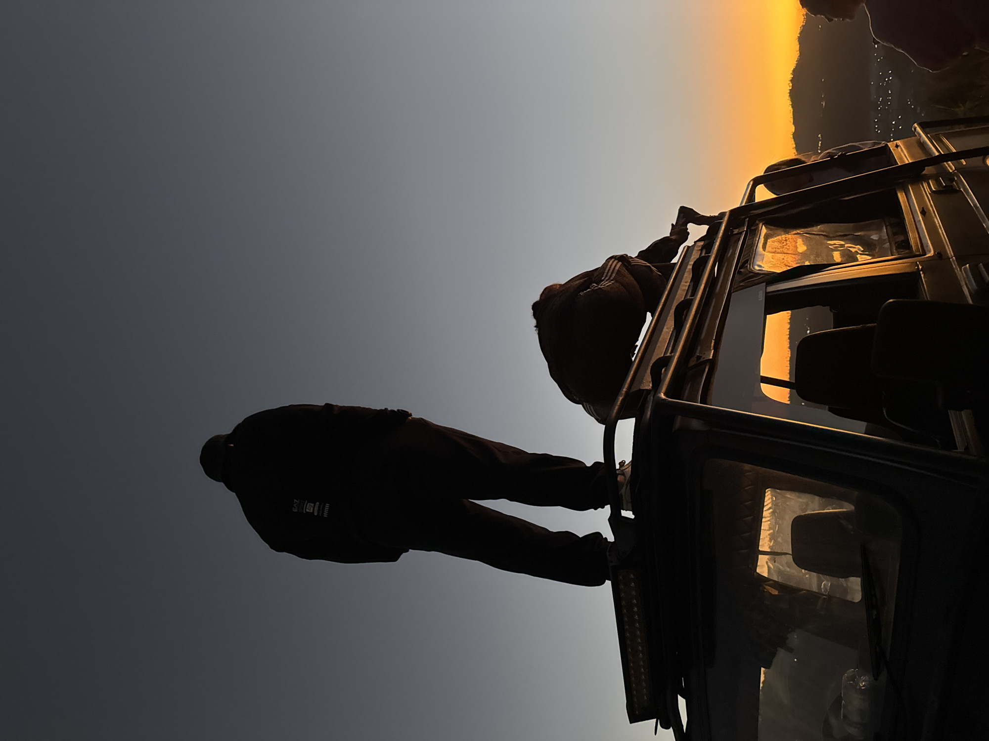 Two figures silhouetted on an SUV rooftop at dusk in Kintamani