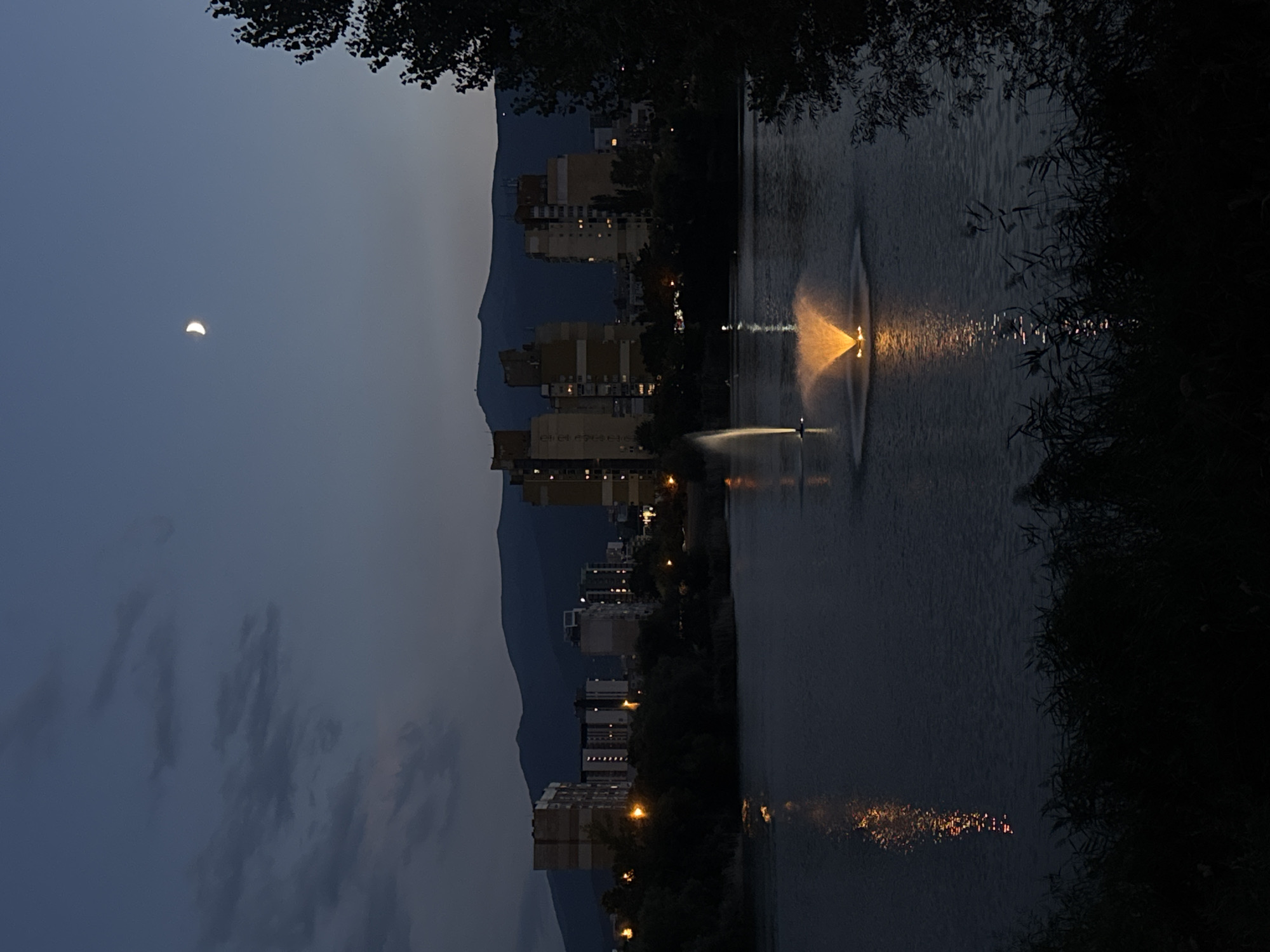 Crescent moon rises over an urban waterway at twilight