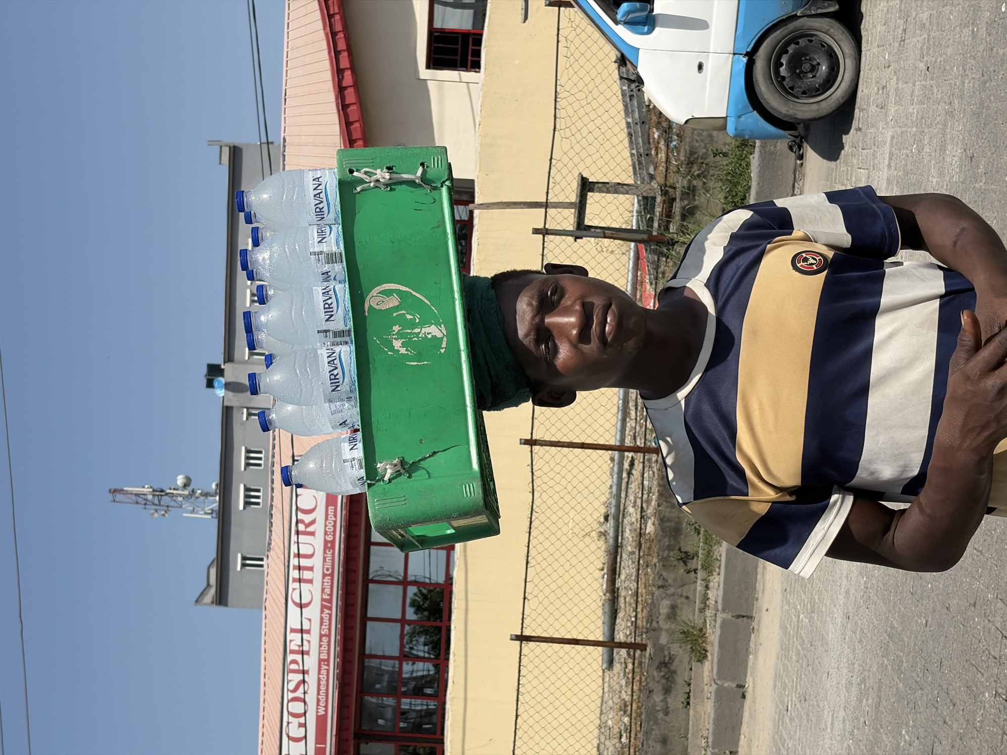 Street vendor carries water bottles in sunny Igboefon, Nigeria