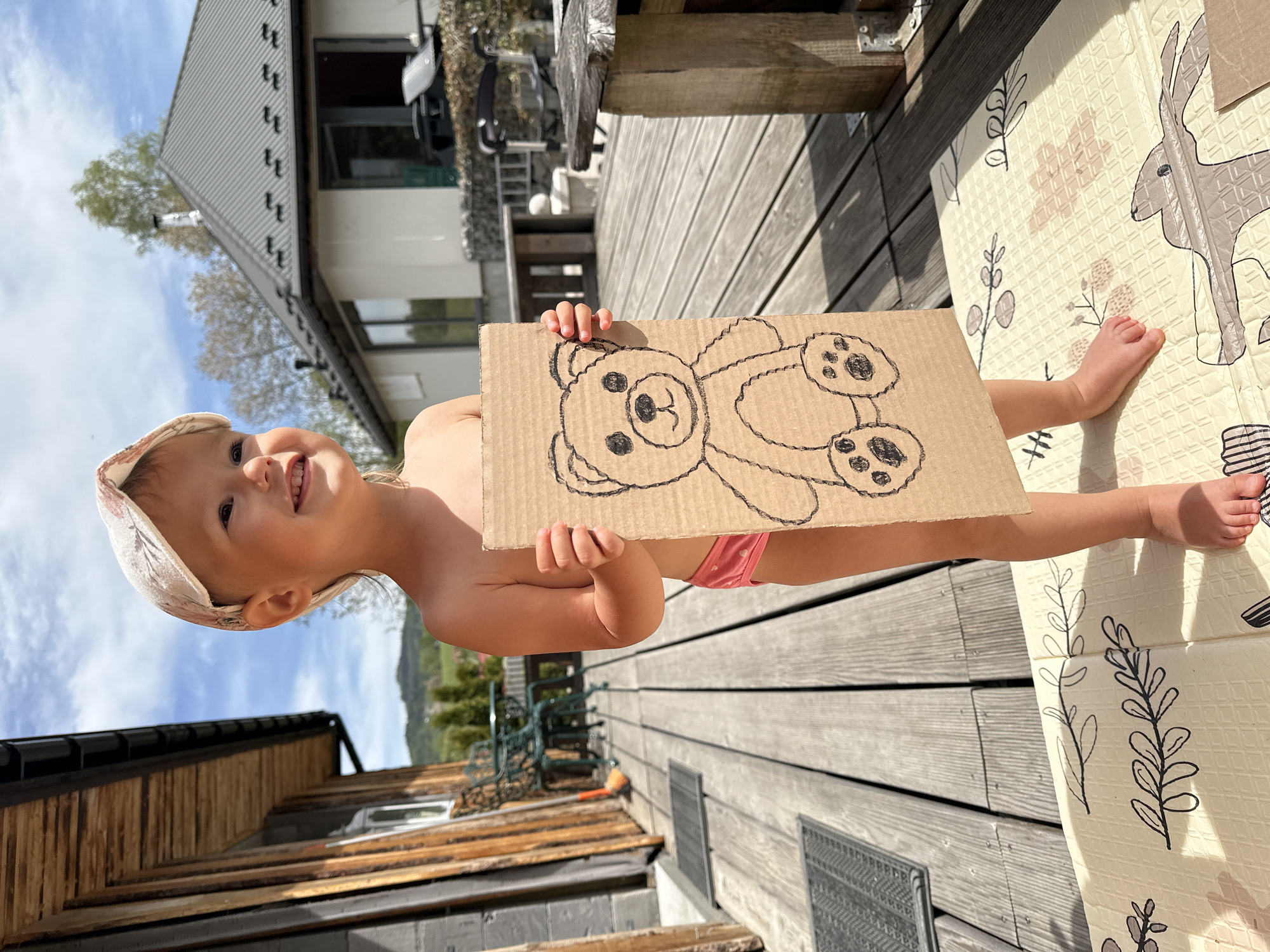 Toddler displays teddy bear drawing on deck in Wisła