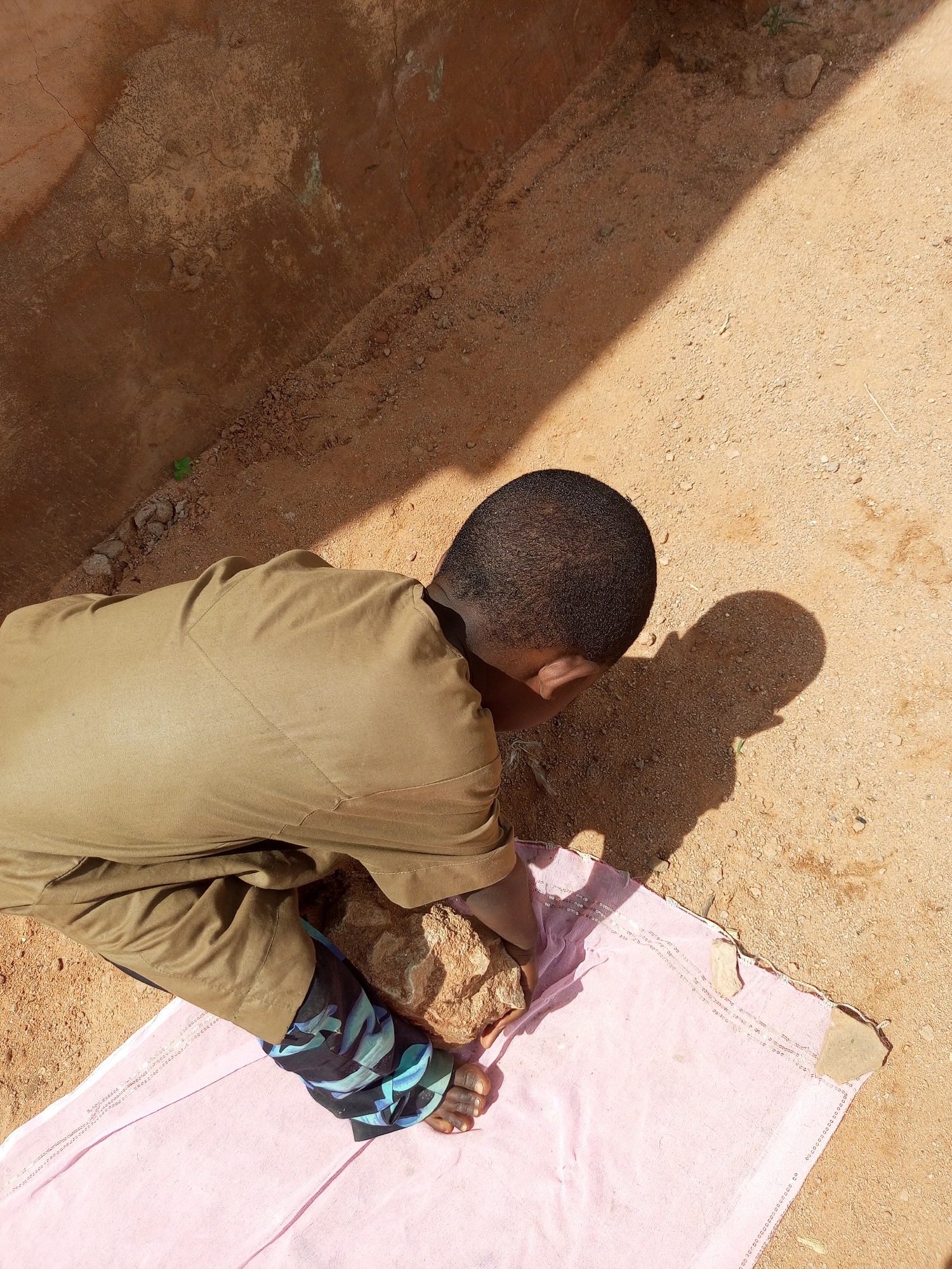 Examining a rock on sandy ground in Gombe, Nigeria
