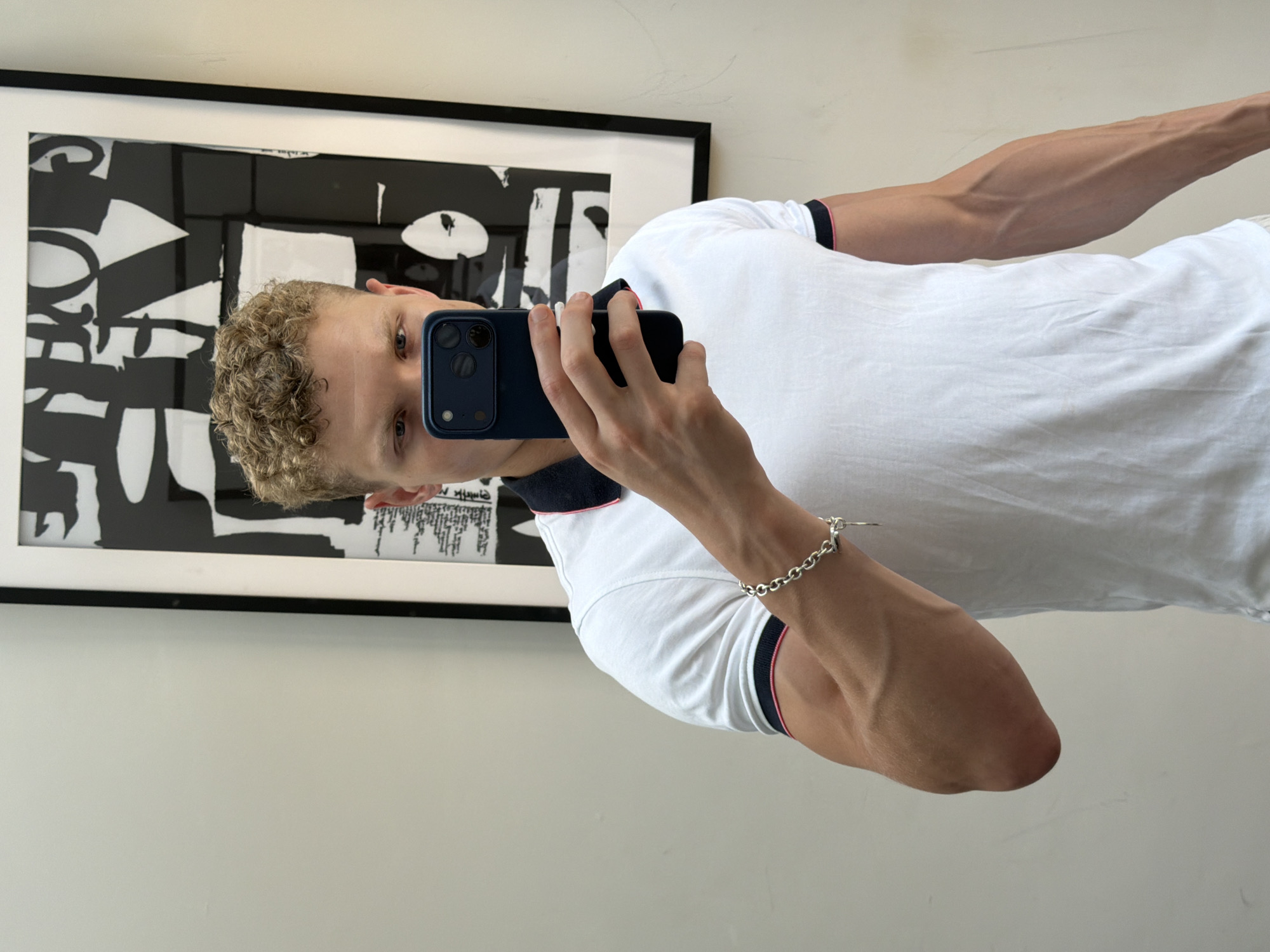 Mirror selfie in a London room, polo shirt and curly hair.