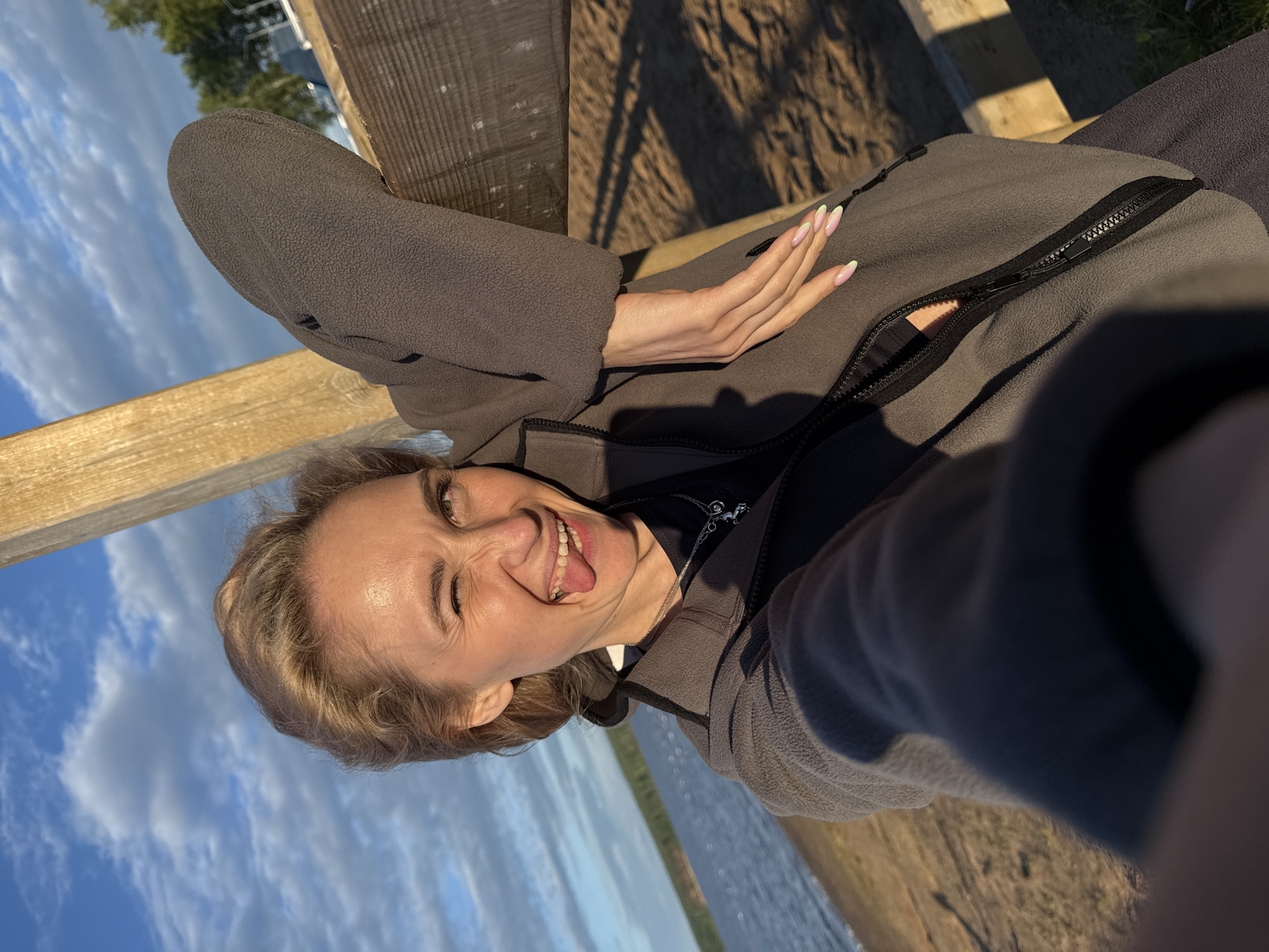 Woman takes playful selfie at Chaykovsky waterfront during golden hour