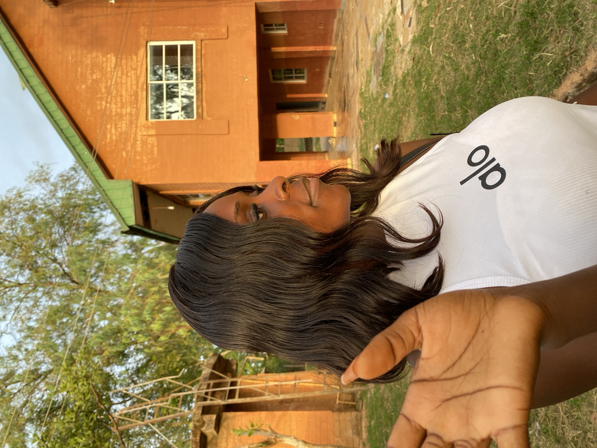 Woman in white shirt rests on grass outside brick building
