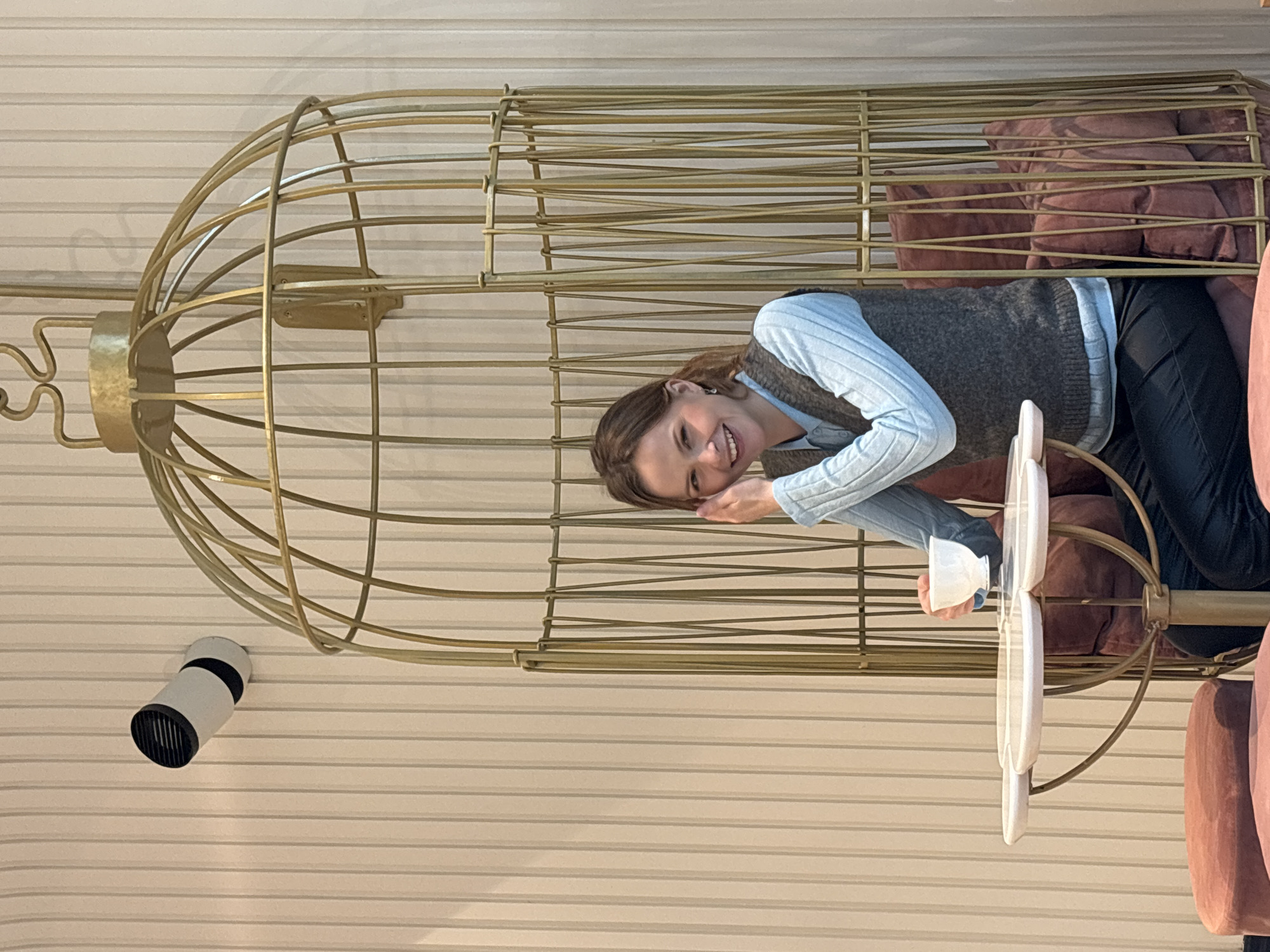 Woman sits in golden birdcage with pillows, Saint Petersburg