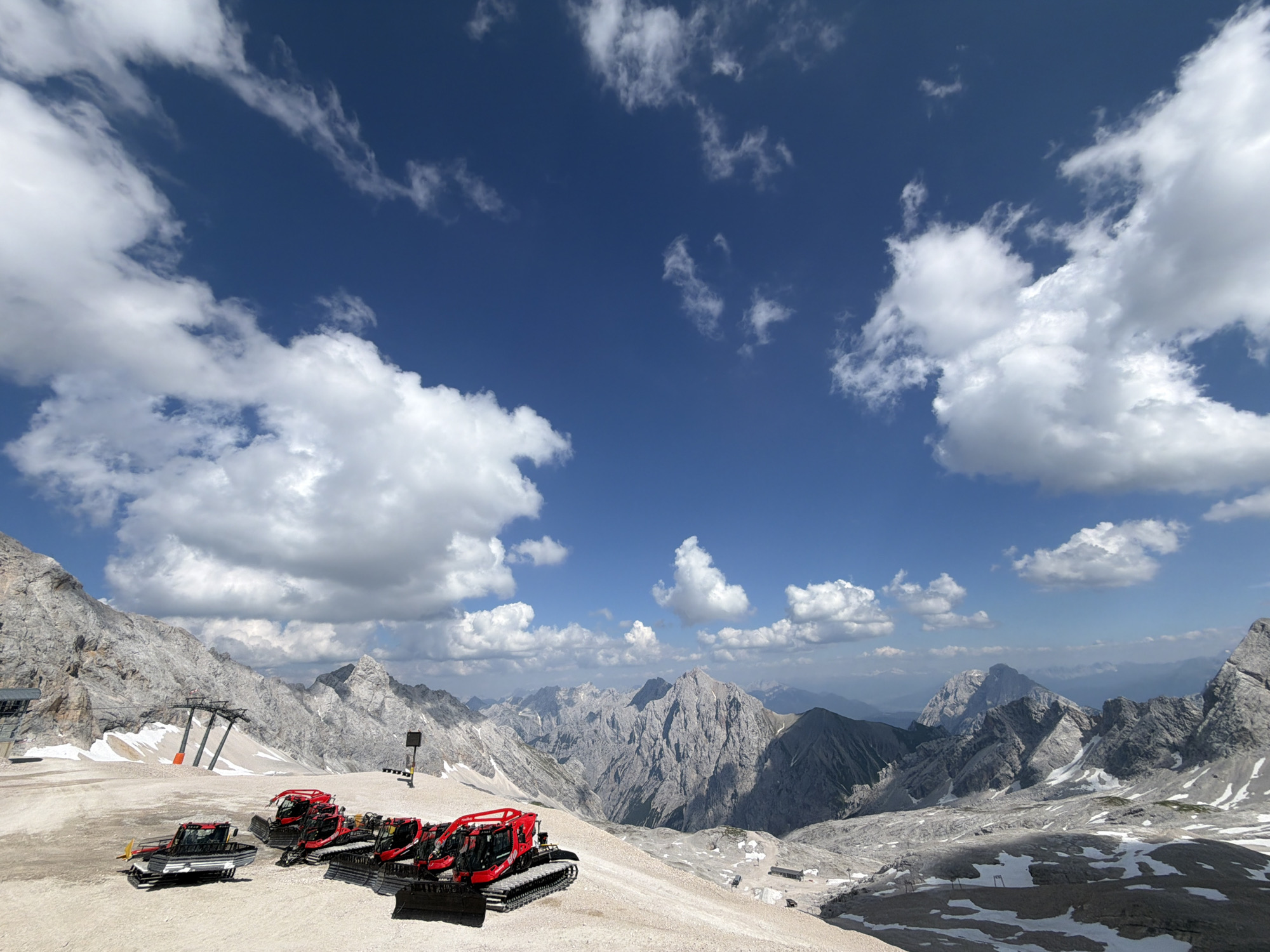Red snowcats parked in the Austrian Alps, late June snow patches visible