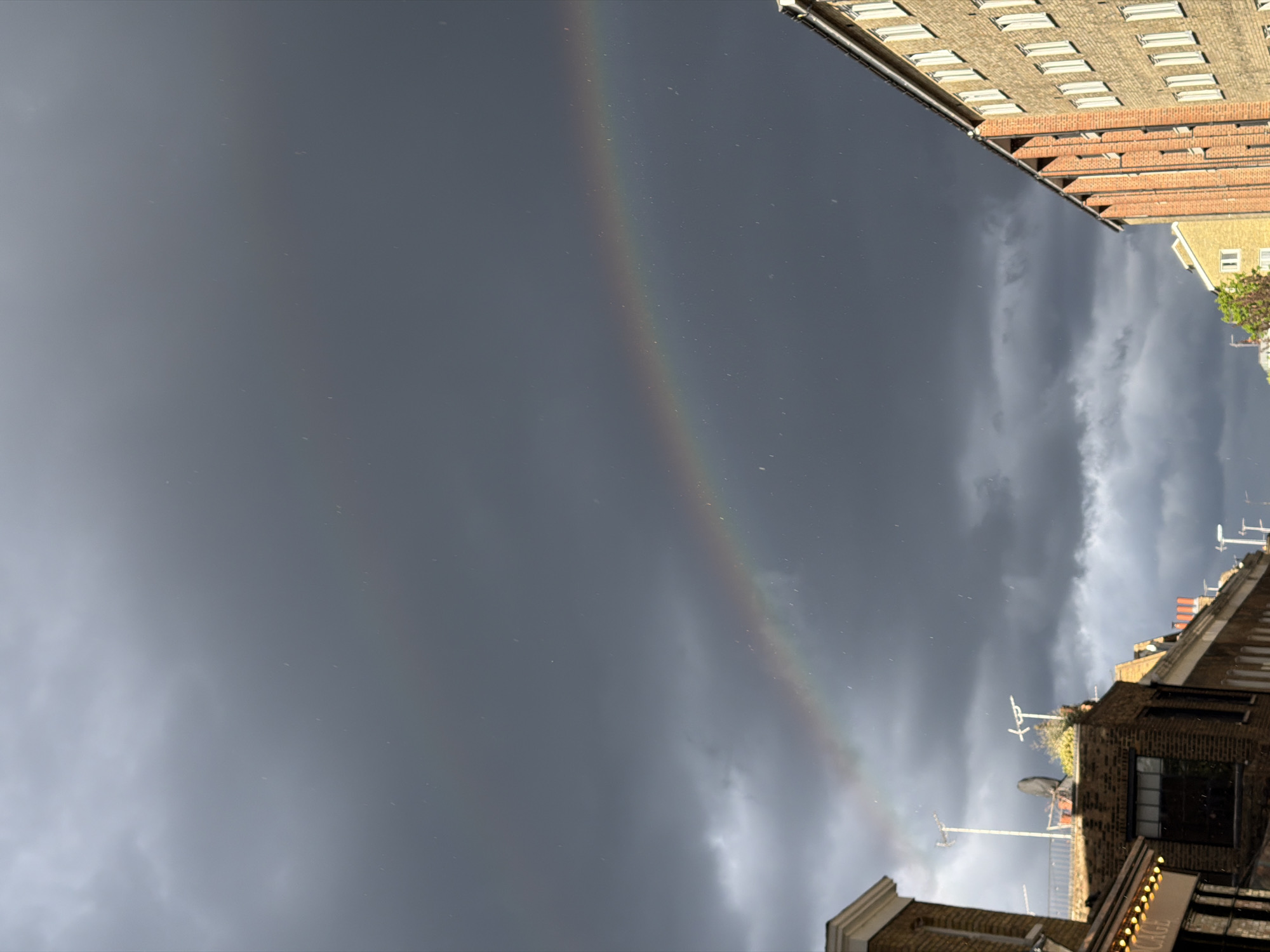 Rainbow appears over London buildings during cloudy evening