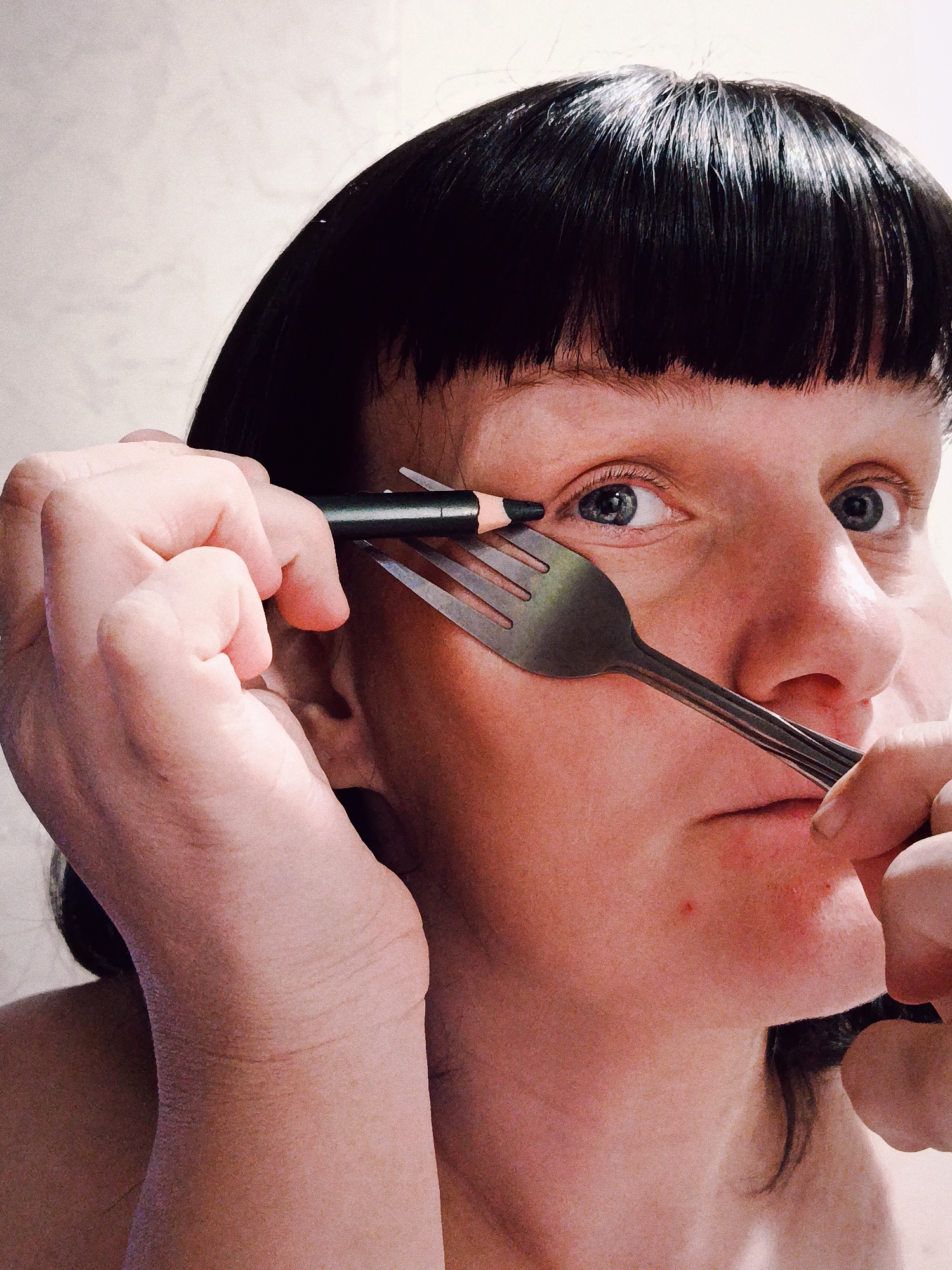 Person holds eyeliner pencil between fork tines near face