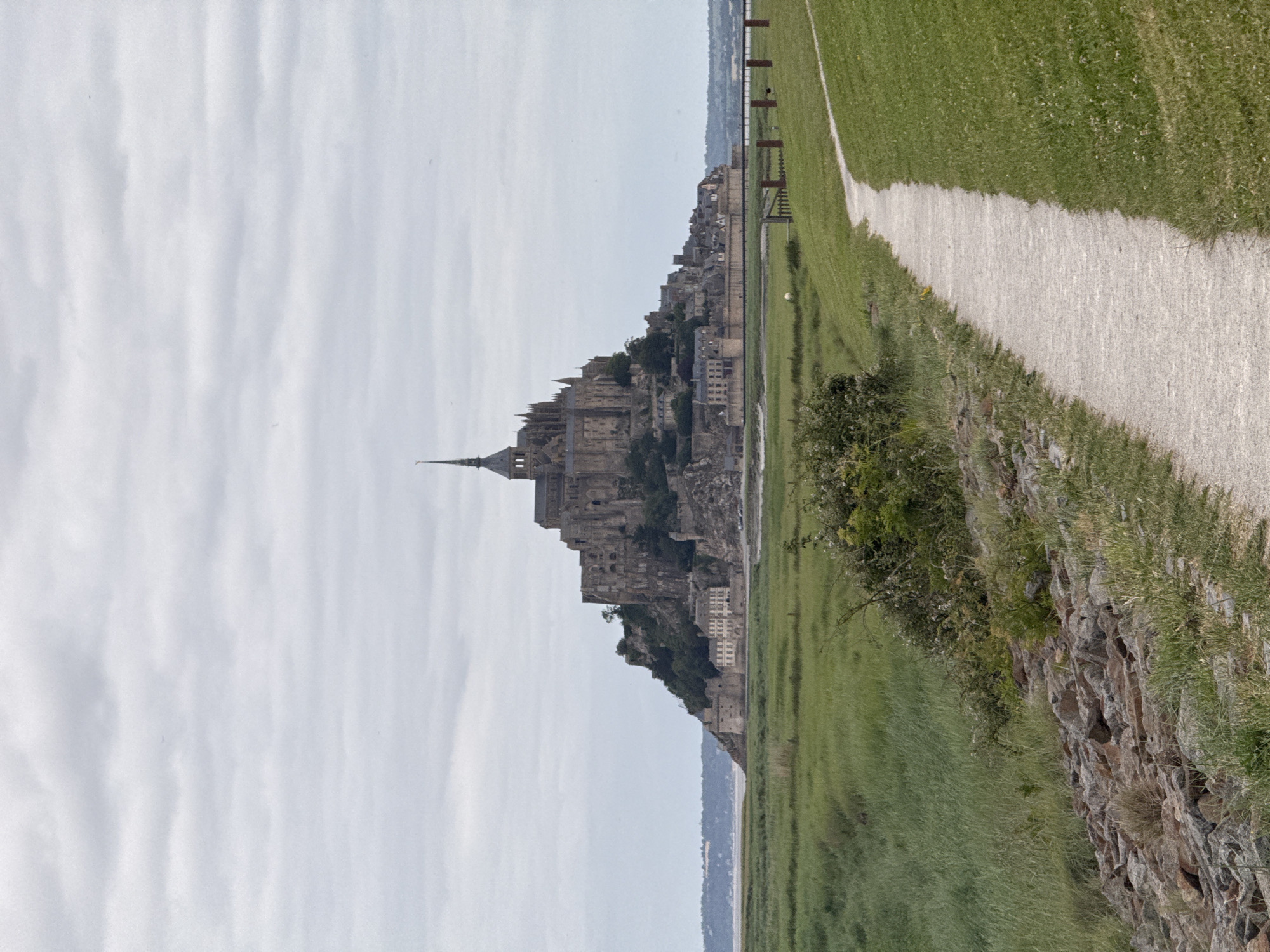 Visitor documents Mont Saint-Michel abbey under overcast skies