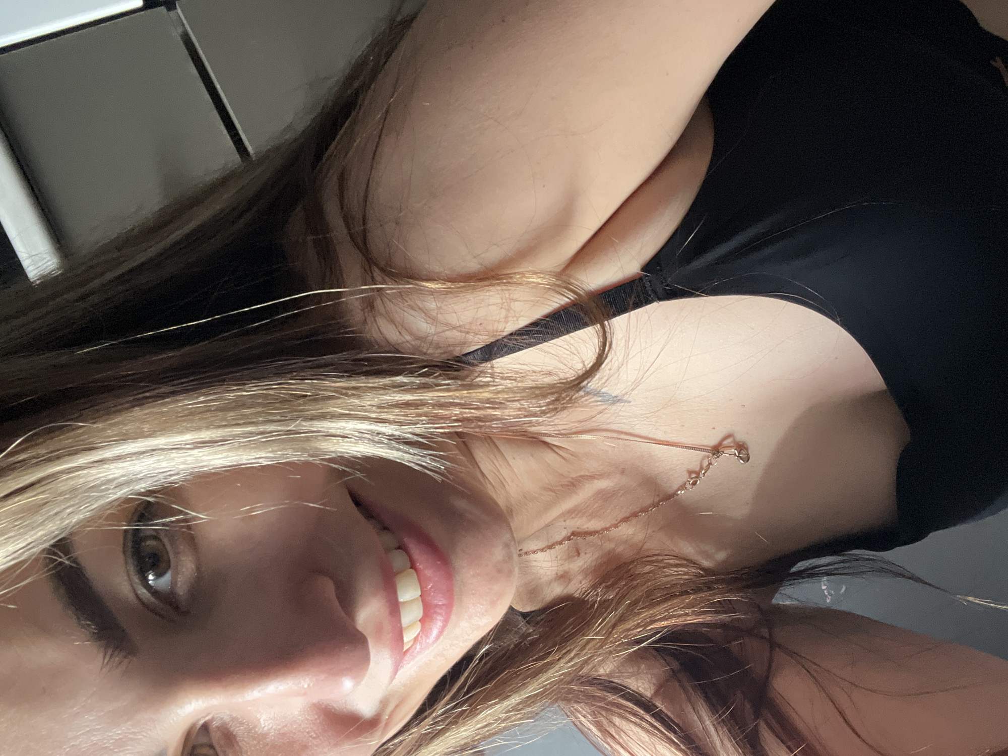 Woman takes selfies wearing black top and gold jewelry
