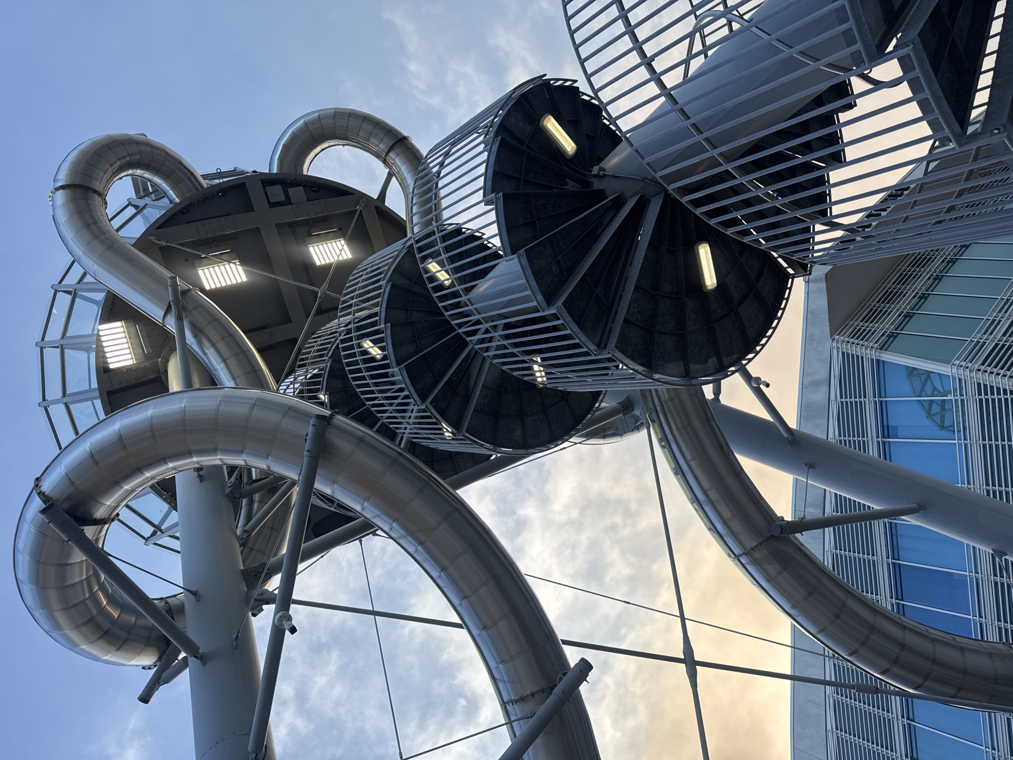 Massive metallic spiral slide structure photographed from below at dusk