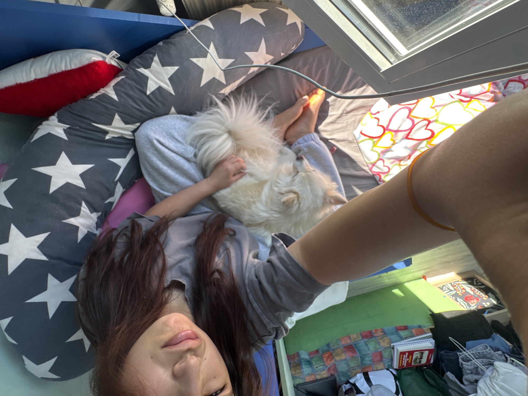 Woman and white dog rest together on heart-patterned bedding