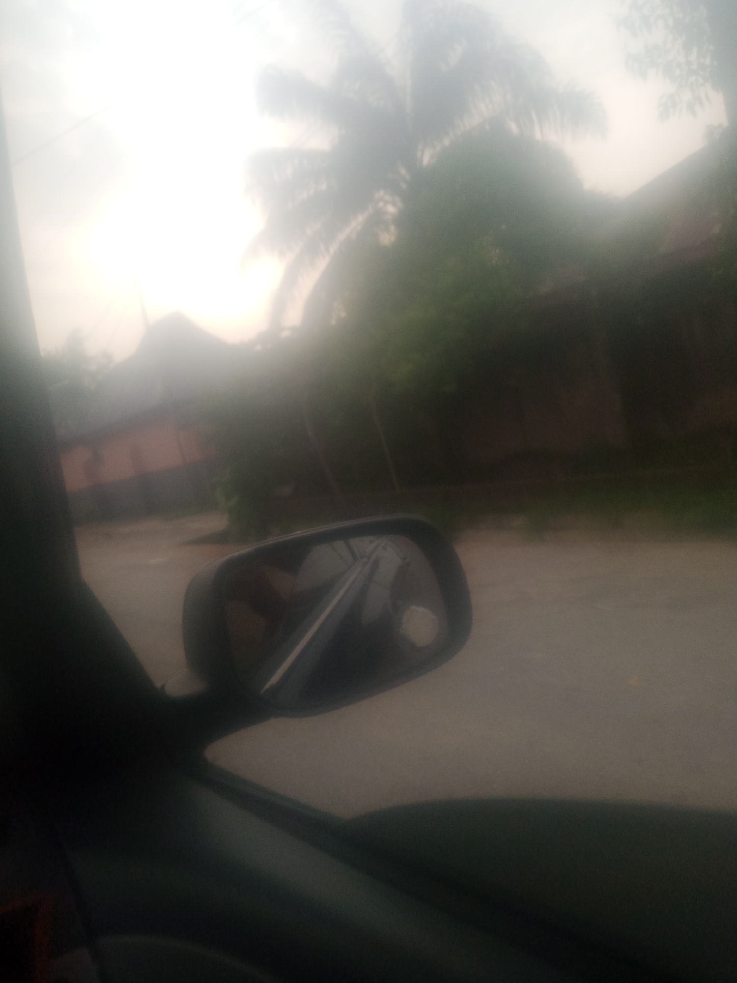 Street-level drive through hazy Jalingo with auto-rickshaw in view