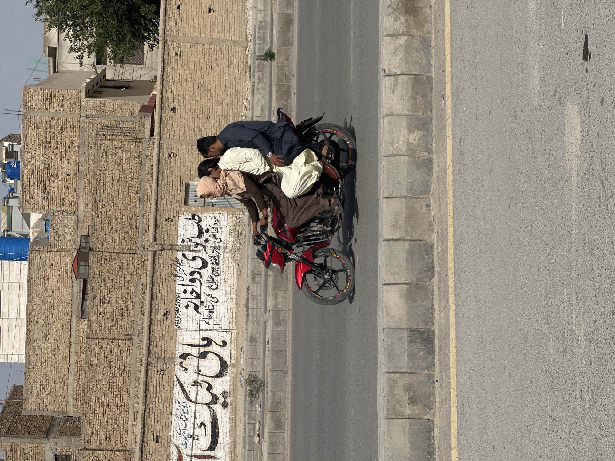 Three men ride red motorcycle in Quetta City