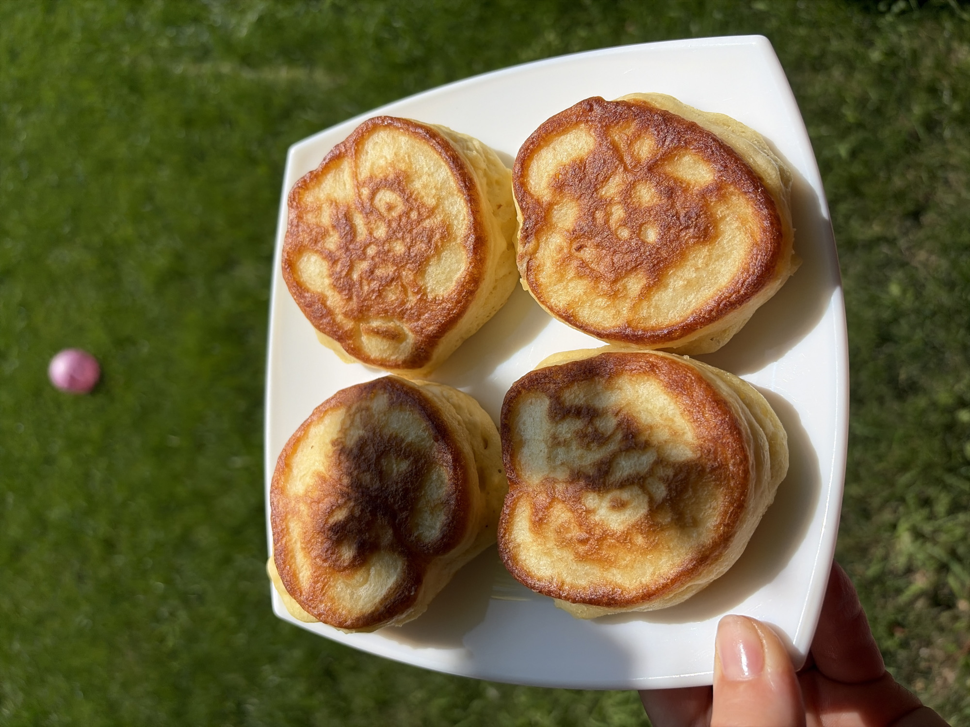 Thick golden pancakes on a white plate, held over green lawn