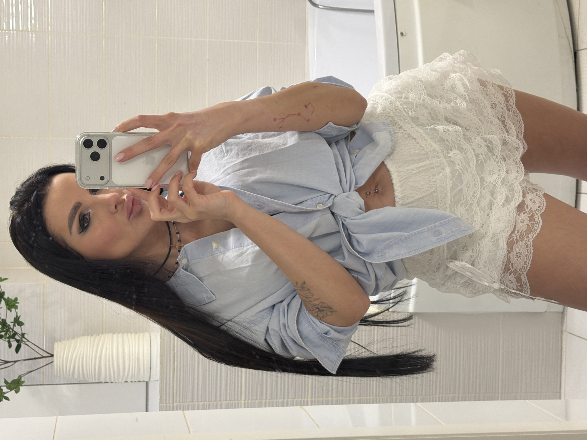 Woman takes bathroom selfie in blue shirt, white skirt