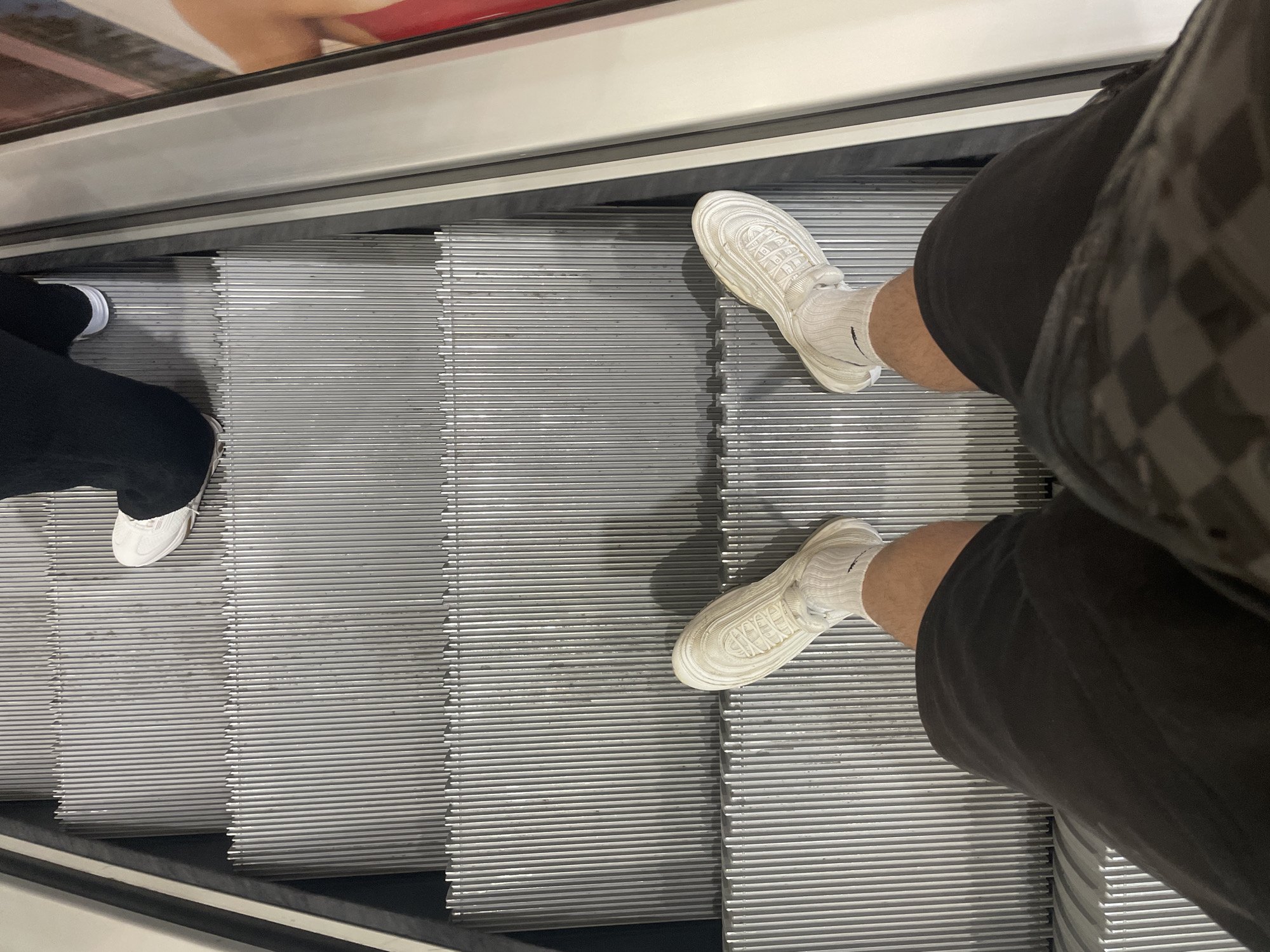 Two people ride escalator in Sofia wearing casual footwear