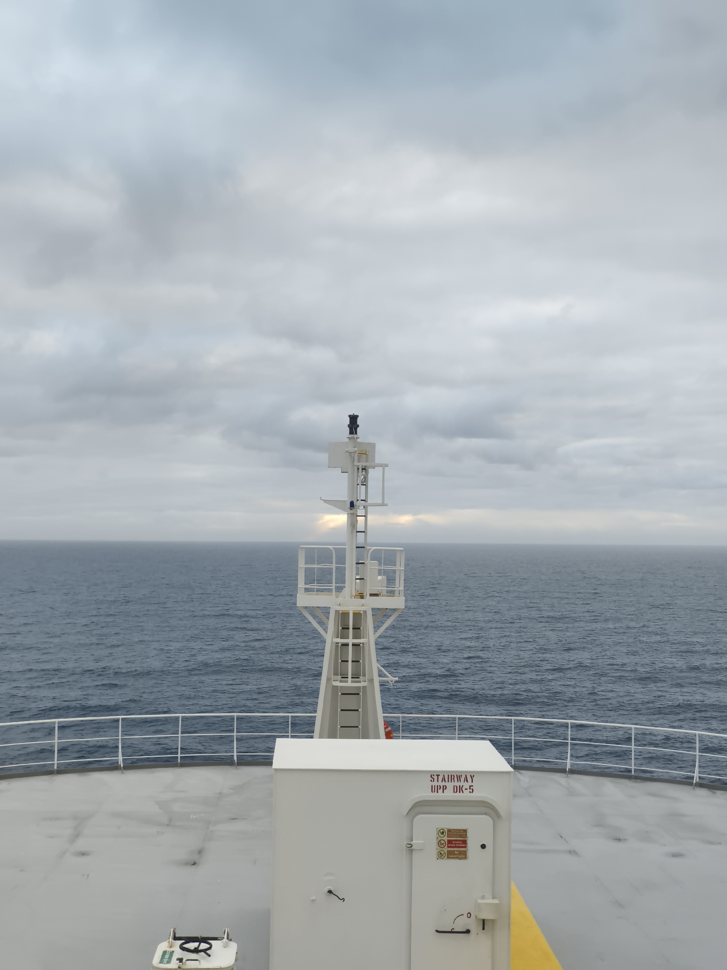 Choppy open sea from a ship's deck, overcast skies and a faint rainbow
