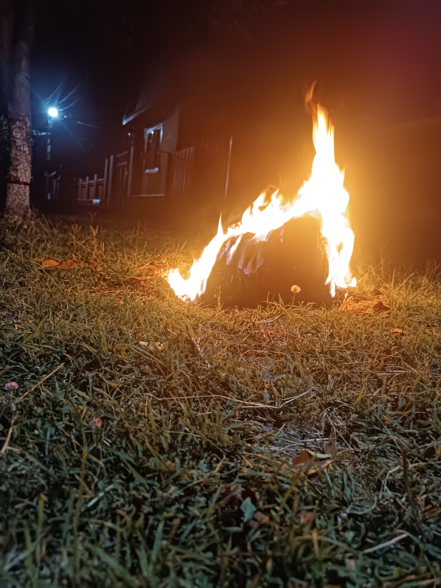 Nighttime bonfire burning in a pit, white car parked nearby