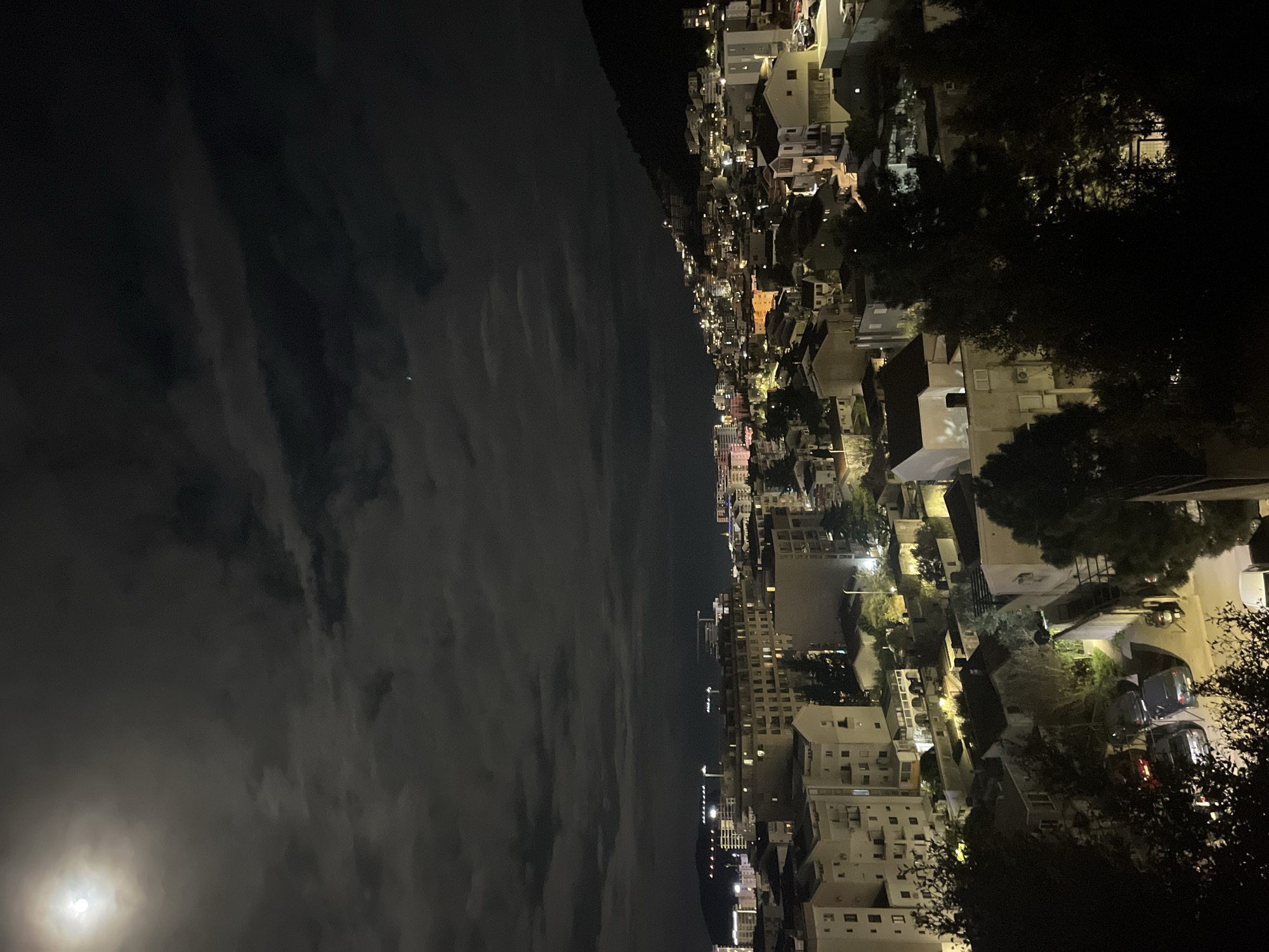 Moon visible over Budva cityscape on cloudy night