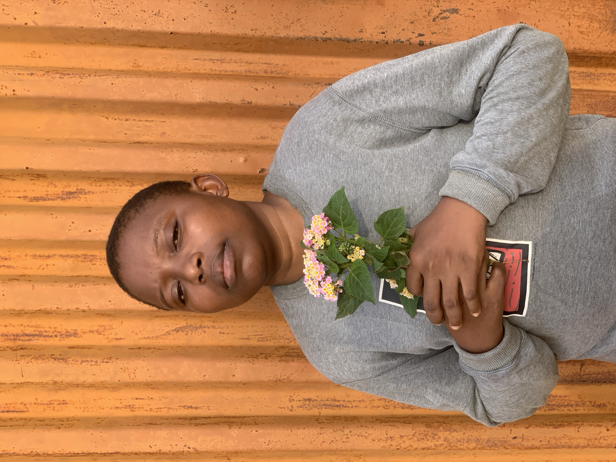 Person with flowers observed resting against wall in Ikorodu