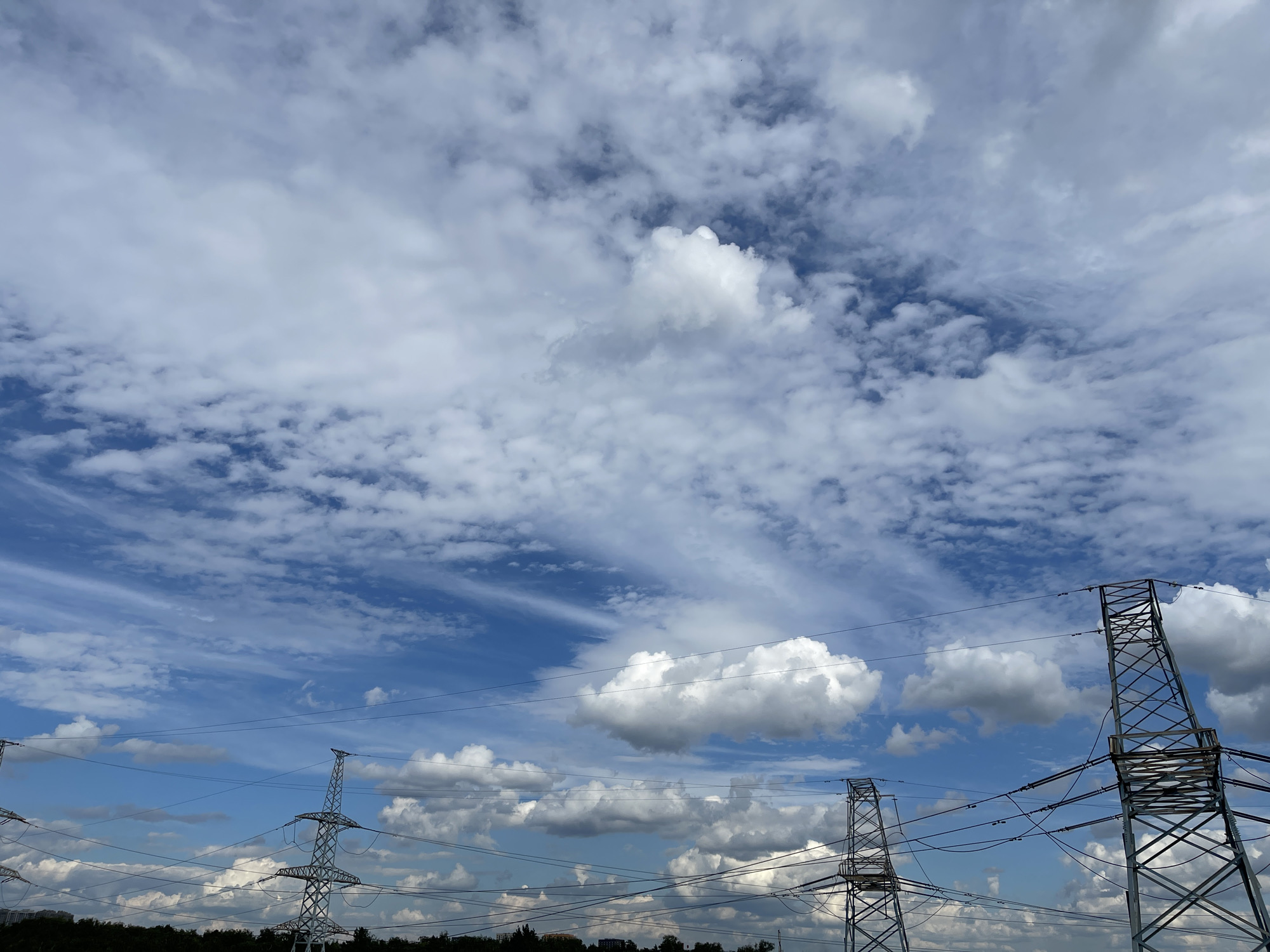 Clouds, power lines, and cityscape under a midday sky