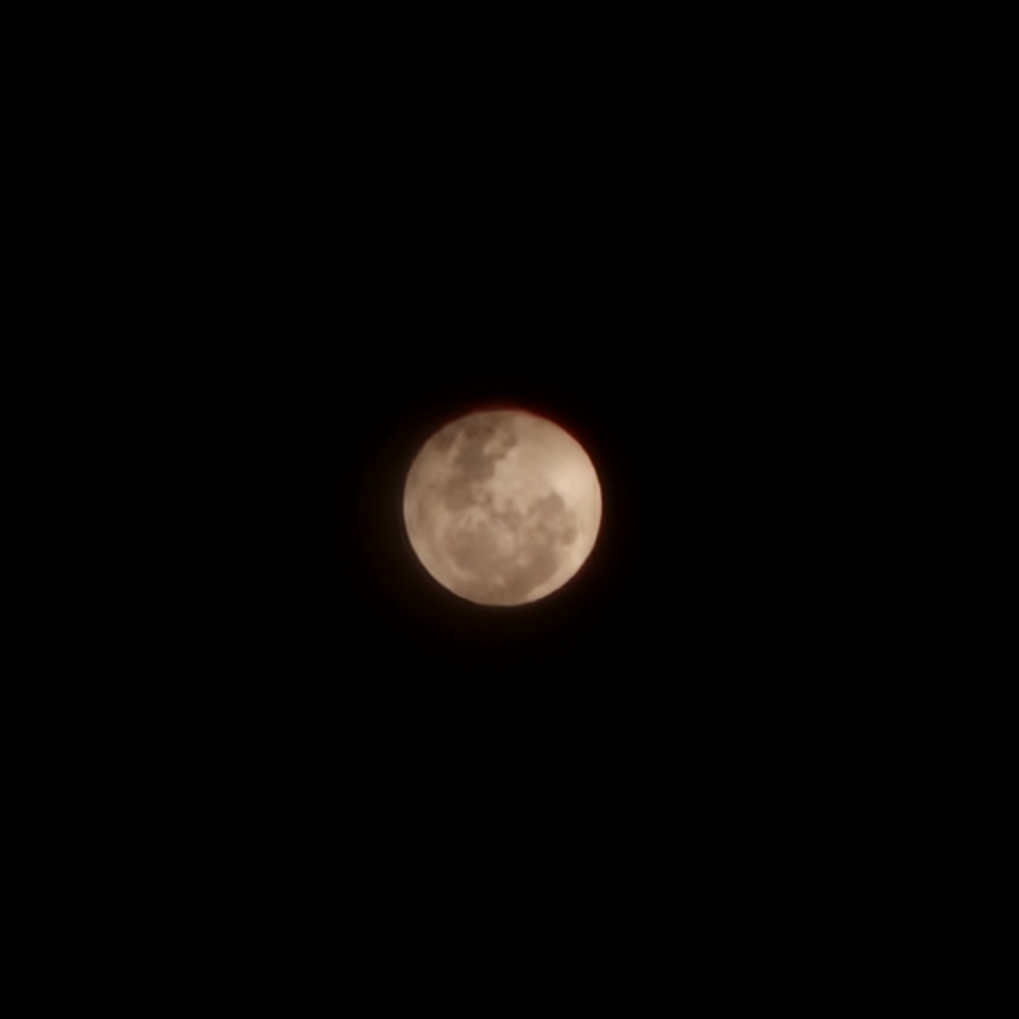 Reddish-orange moon rises through clouds over Basiano
