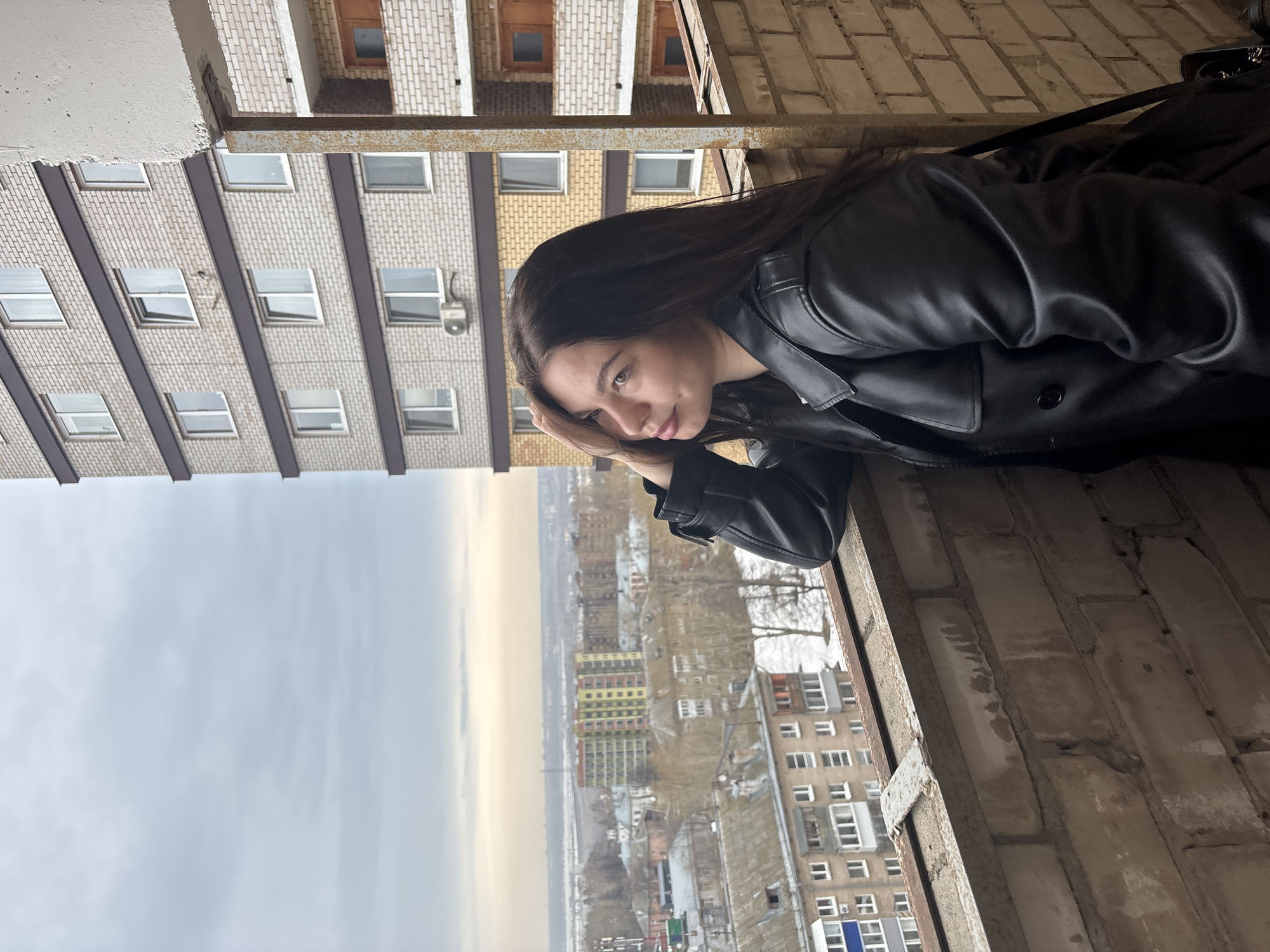 Woman gazes over cityscape from windowsill in Perm