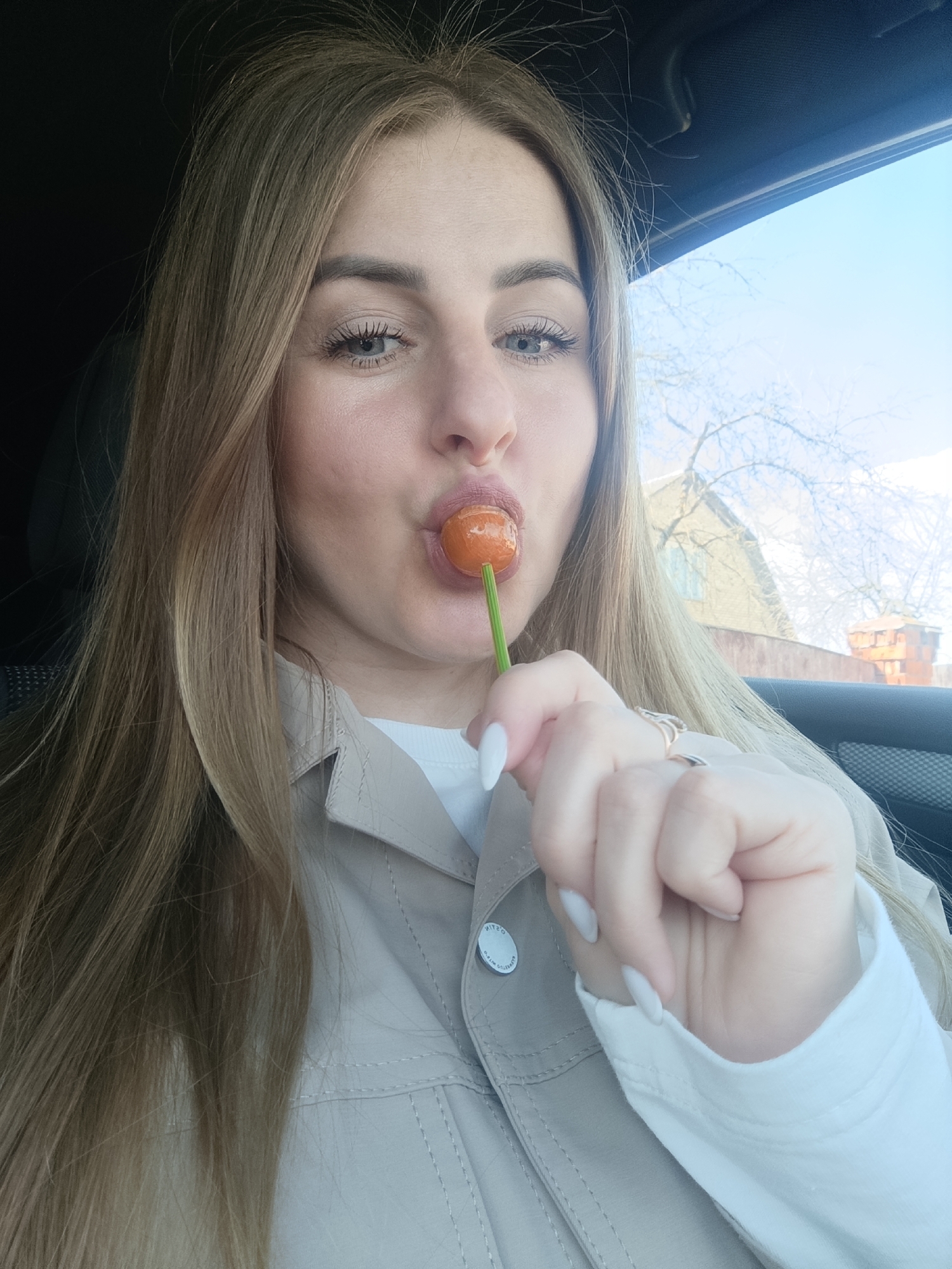 Woman eating orange lollipop while sitting in car
