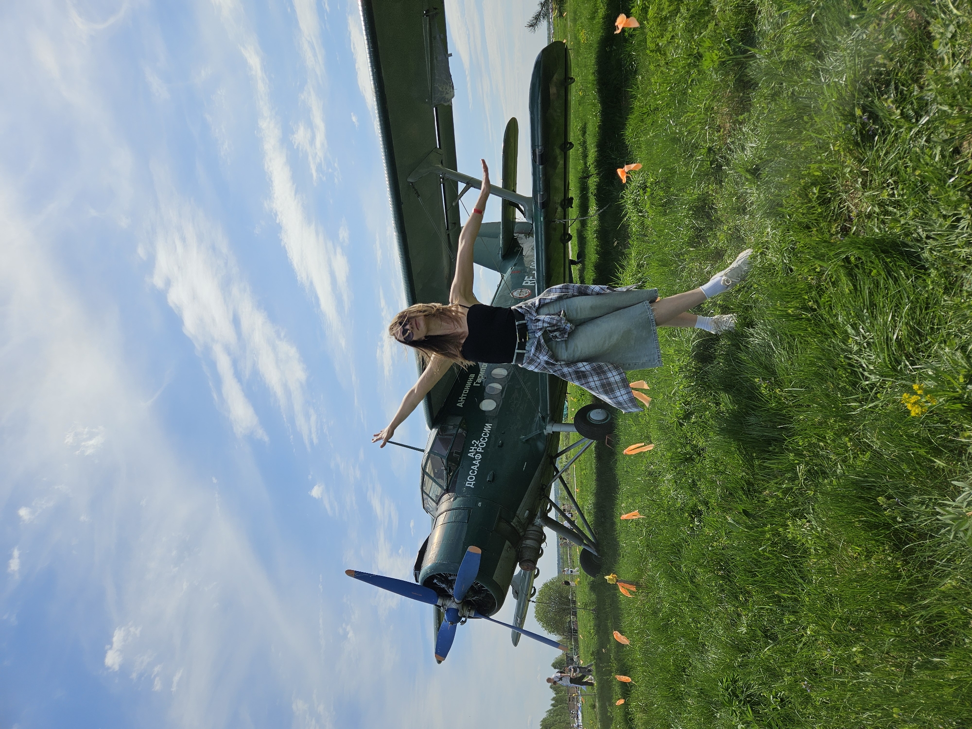 Woman poses with vintage biplane at outdoor event in Izhevsk