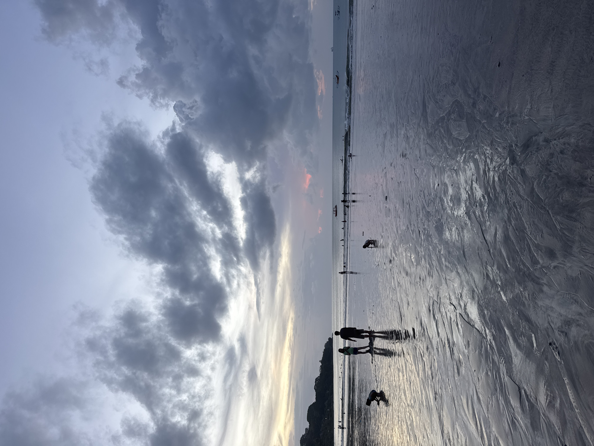 Beach life unfolds during dramatic twilight on coastal shoreline