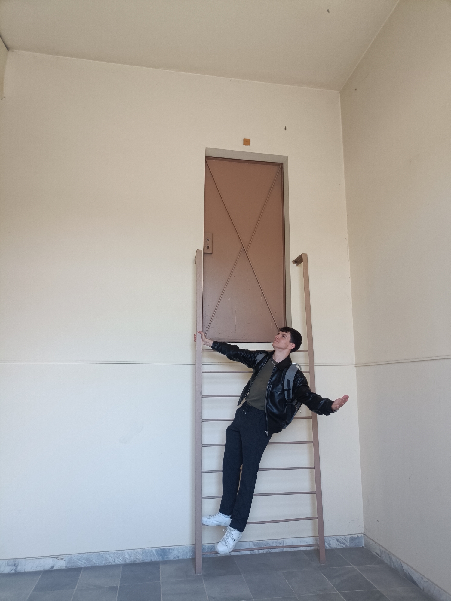 Young man strikes whimsical pose on ladder indoors