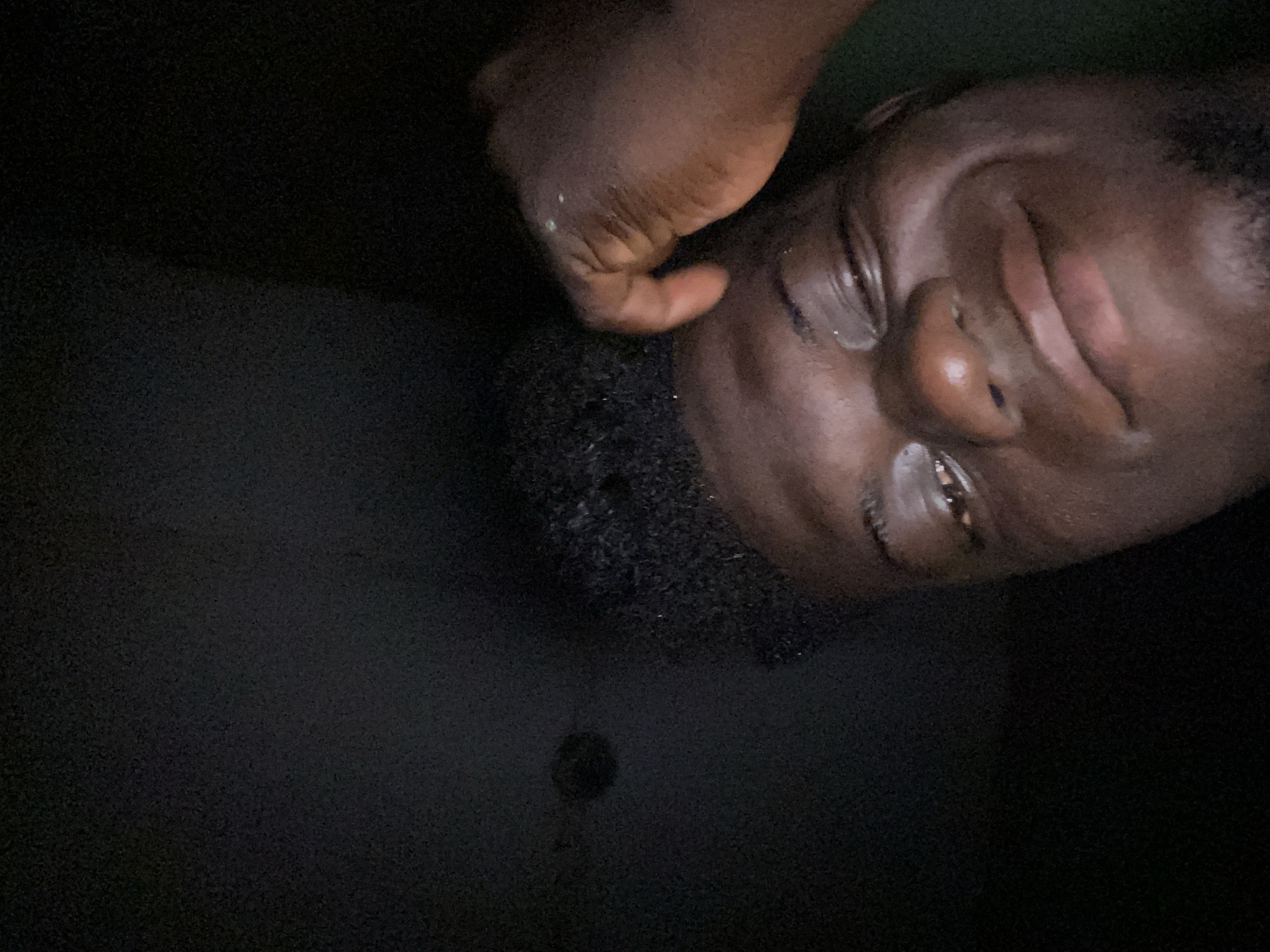 Man observed in dim lighting with hands near face
