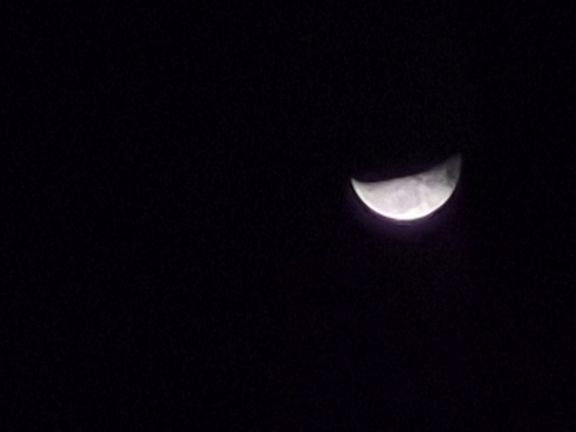 Crescent moon drifts through cloudy skies over rural Estonia
