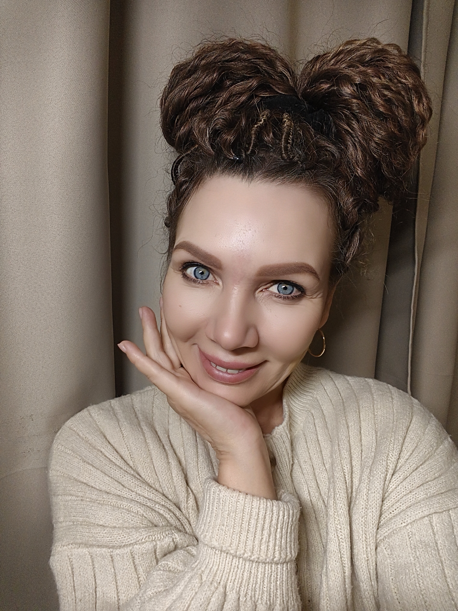 Woman poses for photos in cream sweater and double buns