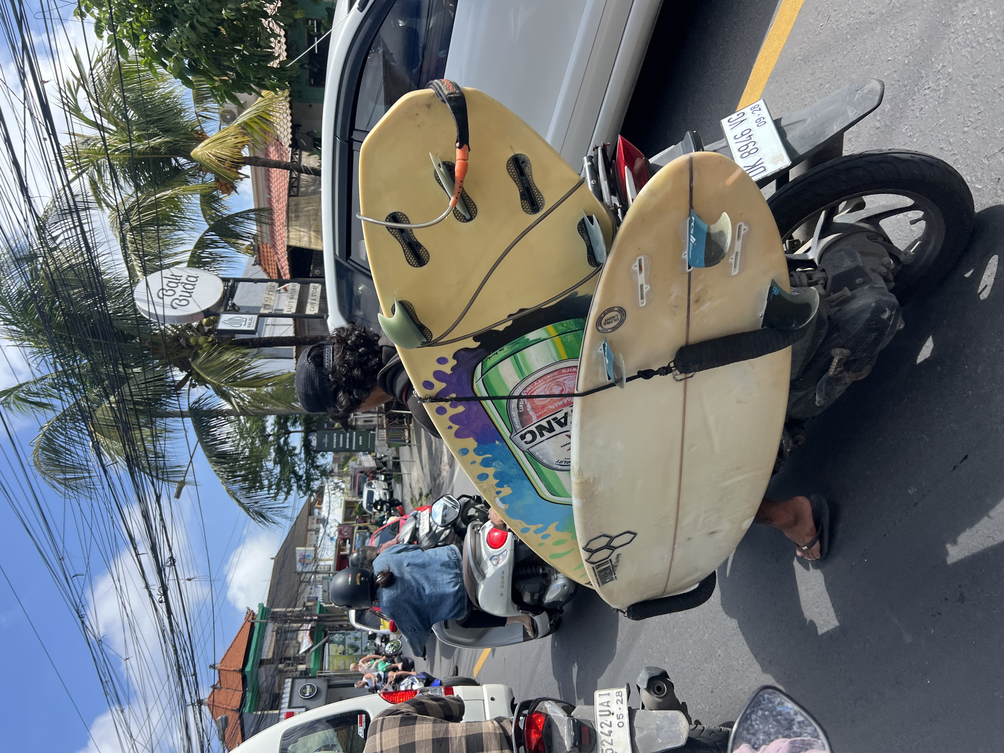 Surfboards strapped to a scooter, weaving through Kuta Selatan traffic